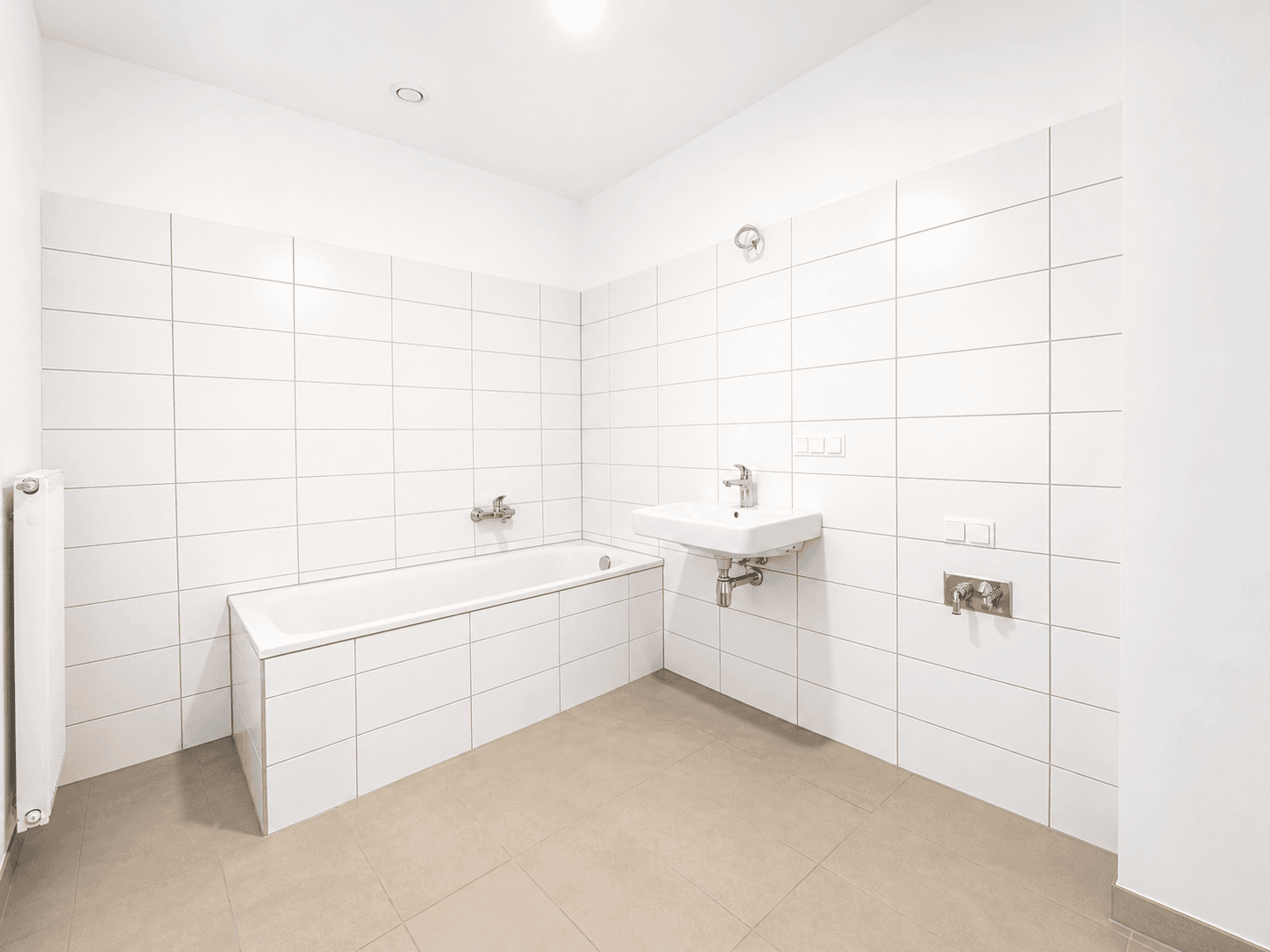 Modernes Badezimmer mit weißen Fliesen, Badewanne und Einzelwaschbecken, in neuwertigem Zustand.