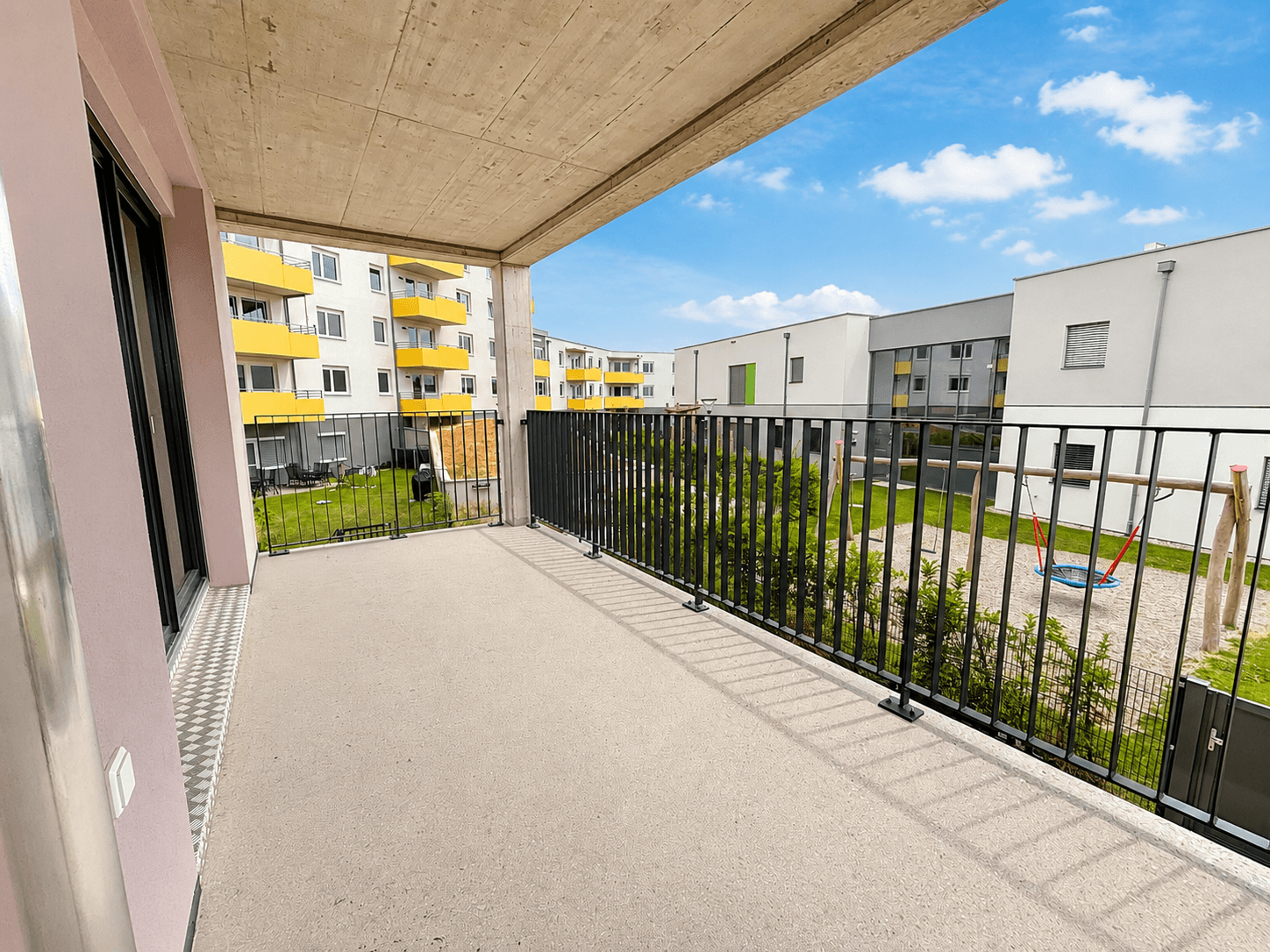Geräumiger Balkon mit Blick auf den Innenhof und einen Spielplatz in einer modernen Wohnanlage.