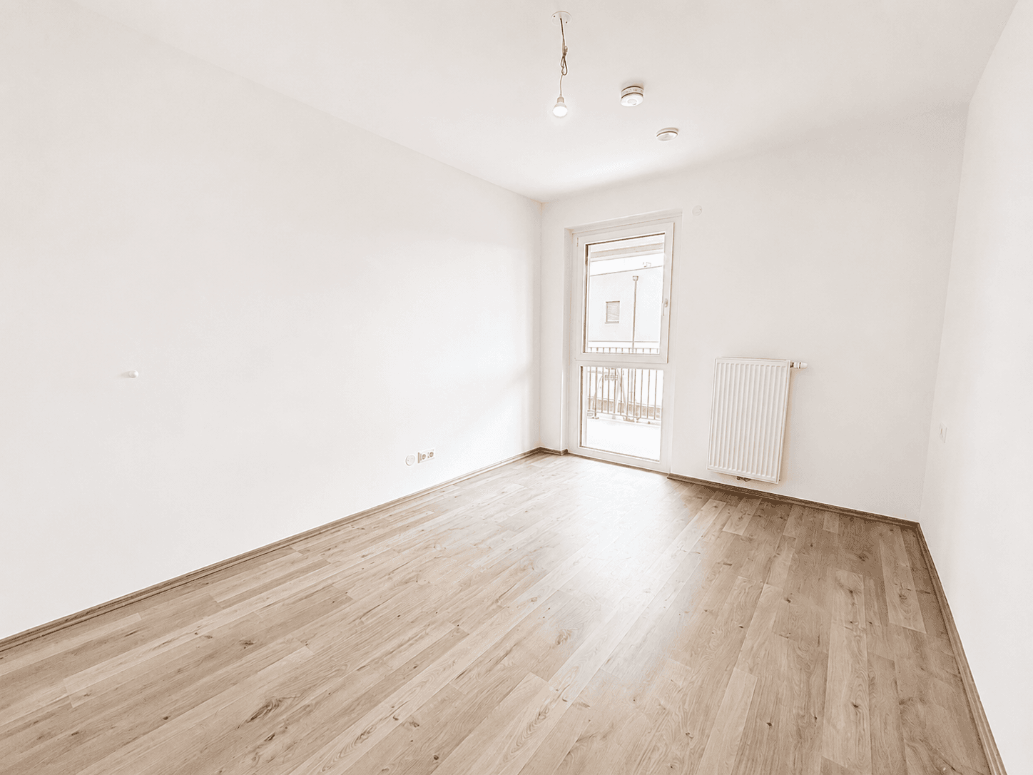 Leeres Schlafzimmer mit hellem Laminatboden, weißen Wänden und Zugang zu einem französischen Balkon.