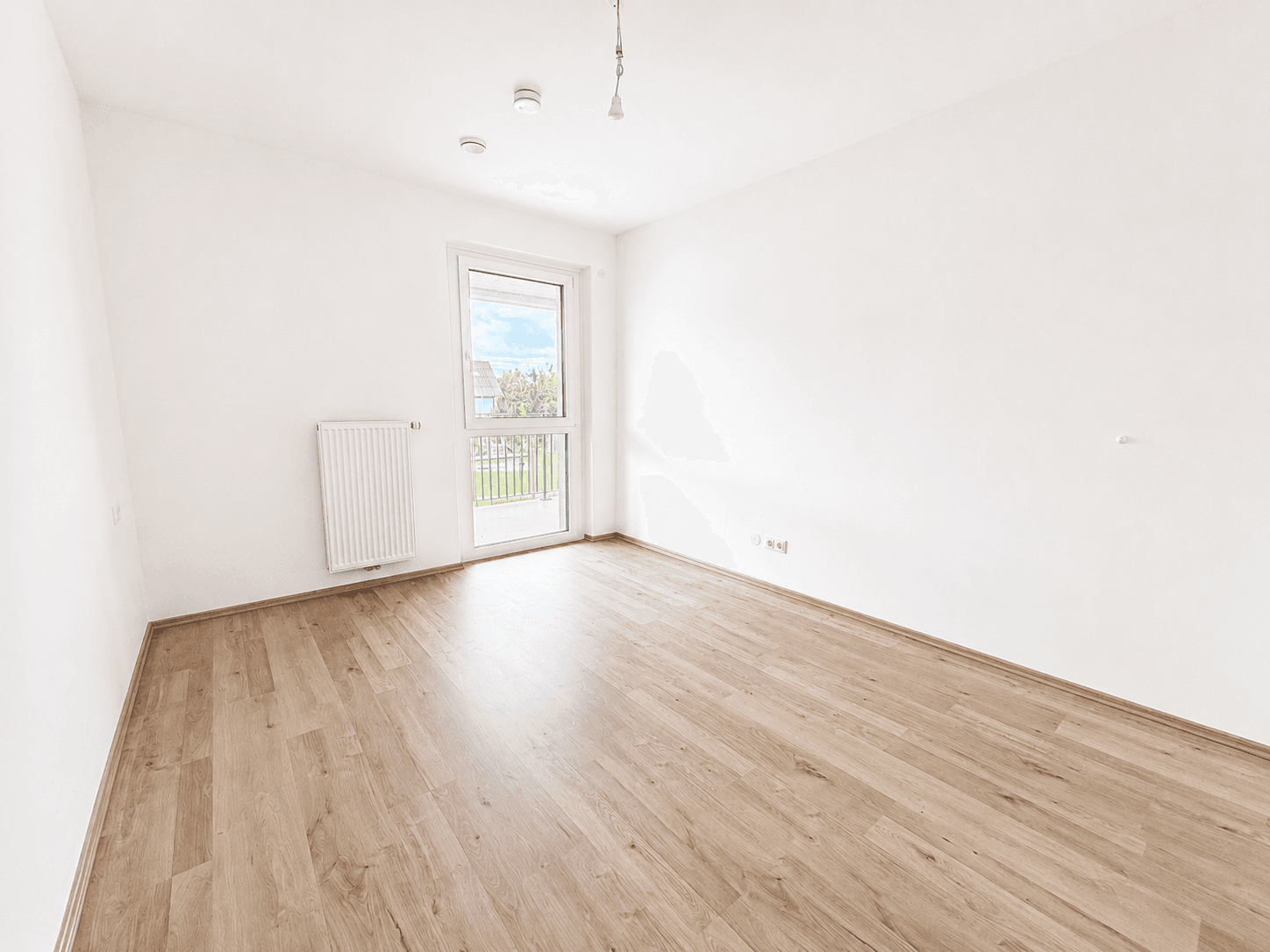 Unmöbliertes Schlafzimmer mit hellem Laminatboden, weißen Wänden und Fenster mit Zugang nach draußen.