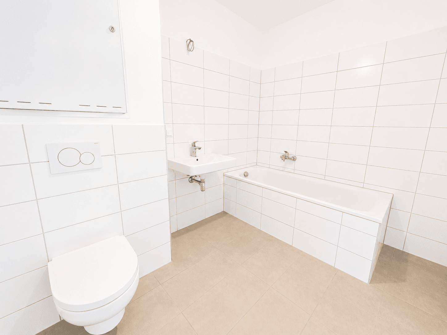 Modernes Badezimmer mit weißen Fliesen, Badewanne, WC und Waschbecken in neuwertigem Zustand.