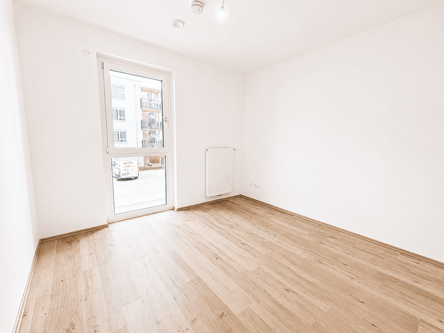 Unmöbliertes Zimmer mit hellem Laminatboden und großem Fenster, bereit zum Einzug.
