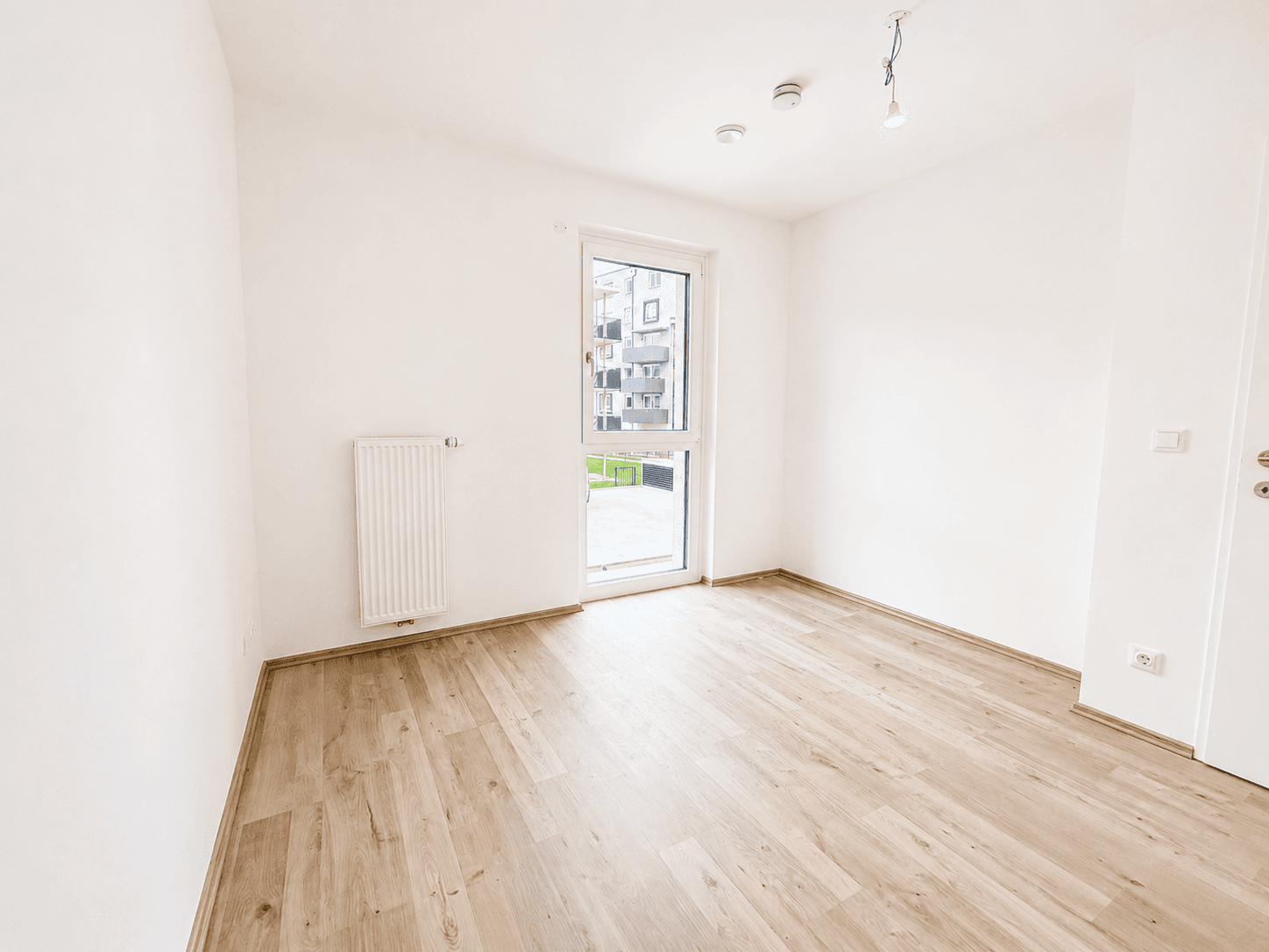 Helles Zimmer mit Laminatboden, weiß gestrichenen Wänden und Blick ins Grüne.