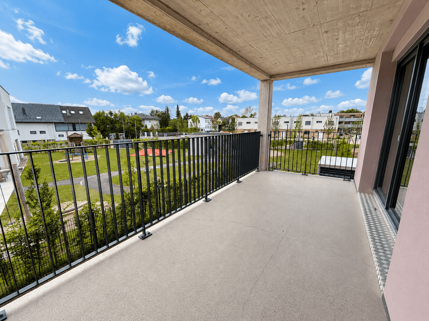 Geräumiger Balkon mit Metallgeländer und Blick auf eine Grünfläche und Spielplatz.