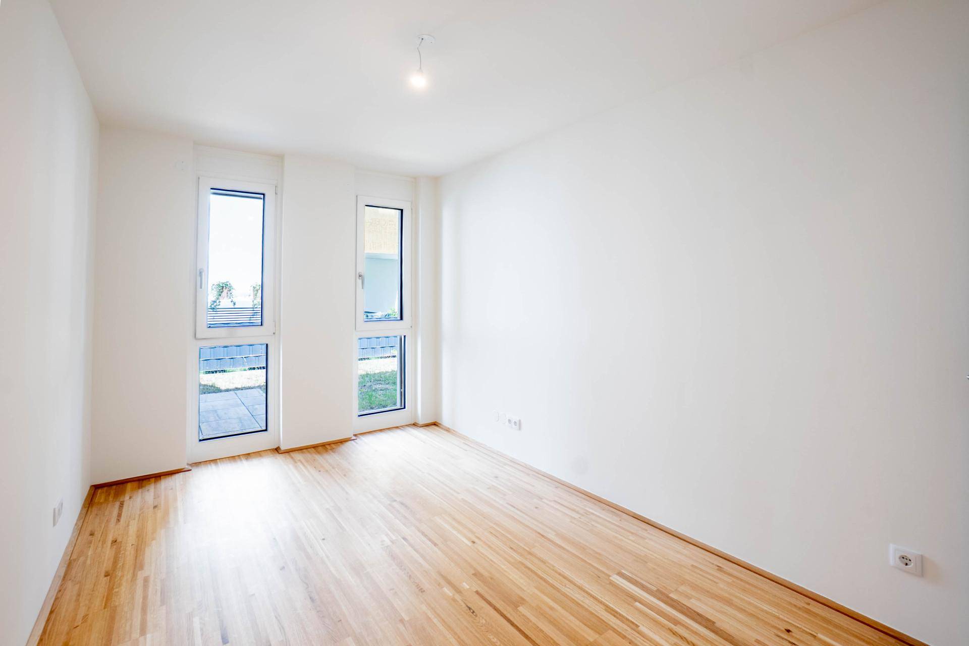Geräumiges Schlafzimmer mit Parkettboden und zwei großen Fenstern mit Balkonzugang.