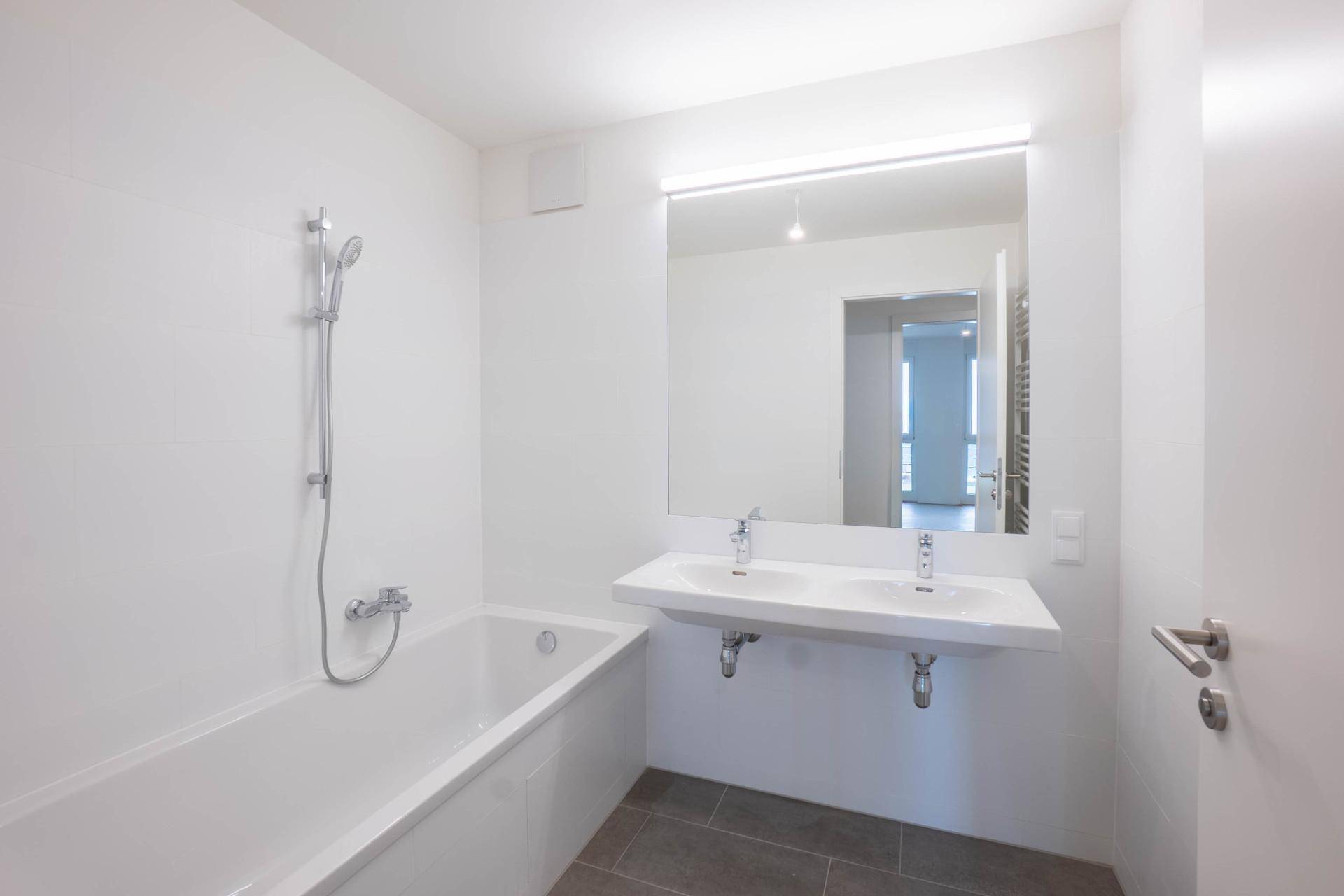 Modernes Badezimmer mit Badewanne, Doppelwaschbecken und großem Spiegel.