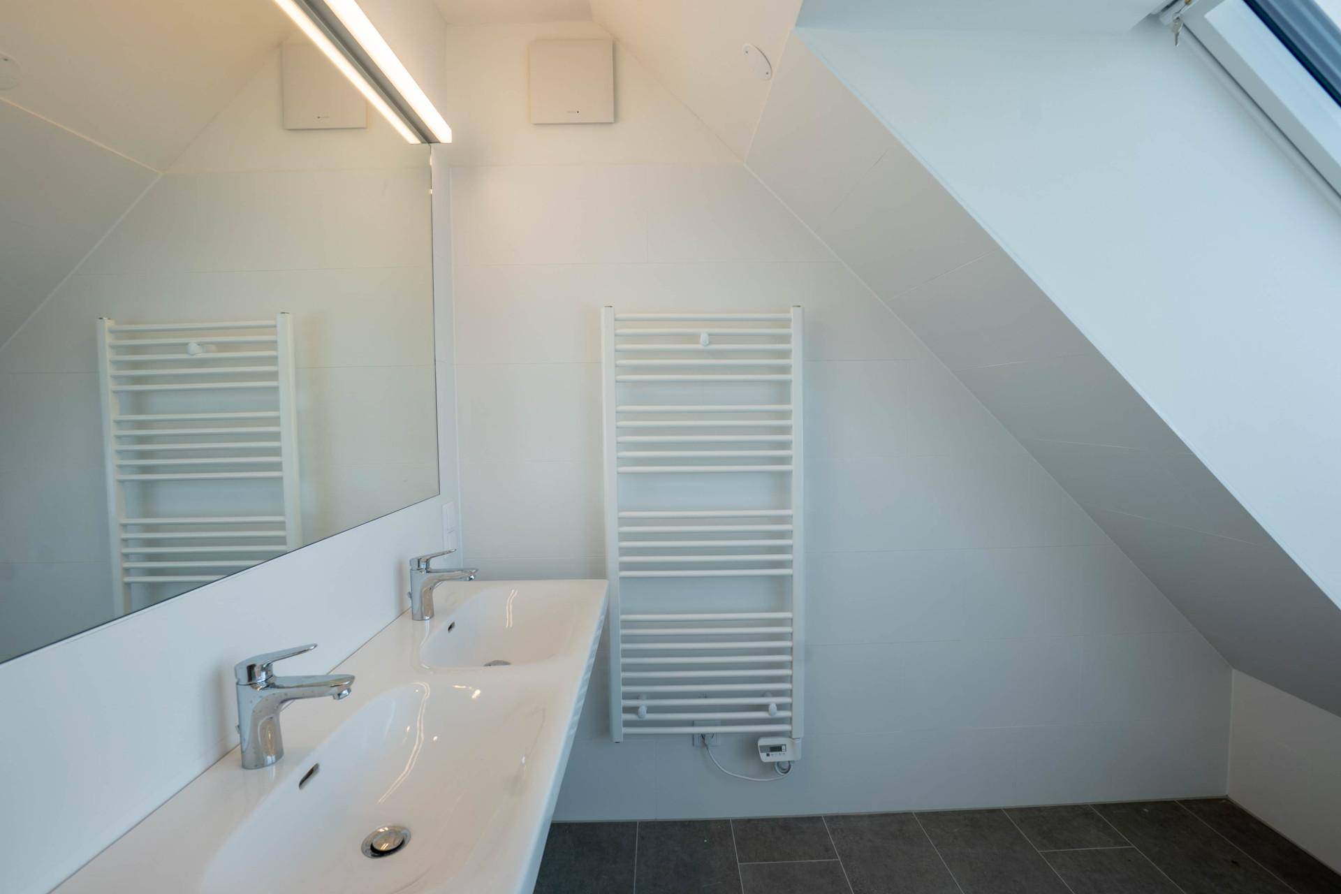 Modernes Badezimmer mit Doppelwaschbecken, großem Spiegel und beheiztem Handtuchhalter.