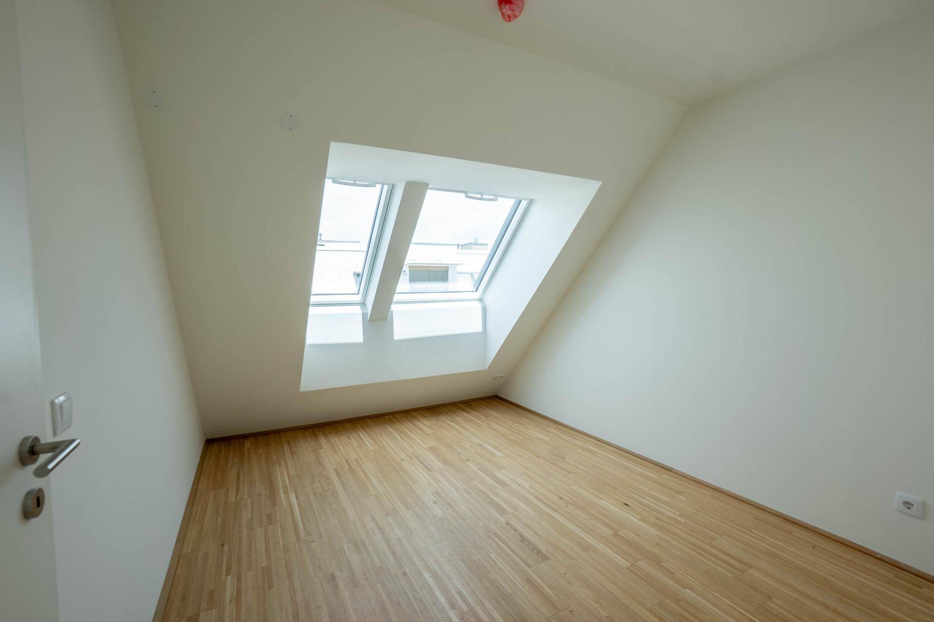 Helles Schlafzimmer mit Holzboden, schrägen Wänden und einem großen Dachfenster.