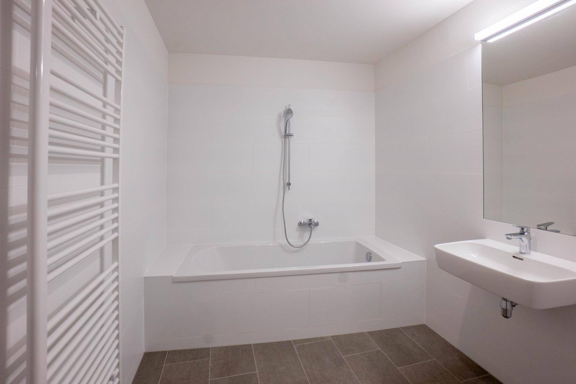 Modernes Badezimmer mit Badewanne, Einzelwaschbecken, beheiztem Handtuchhalter und grauen Fliesen.