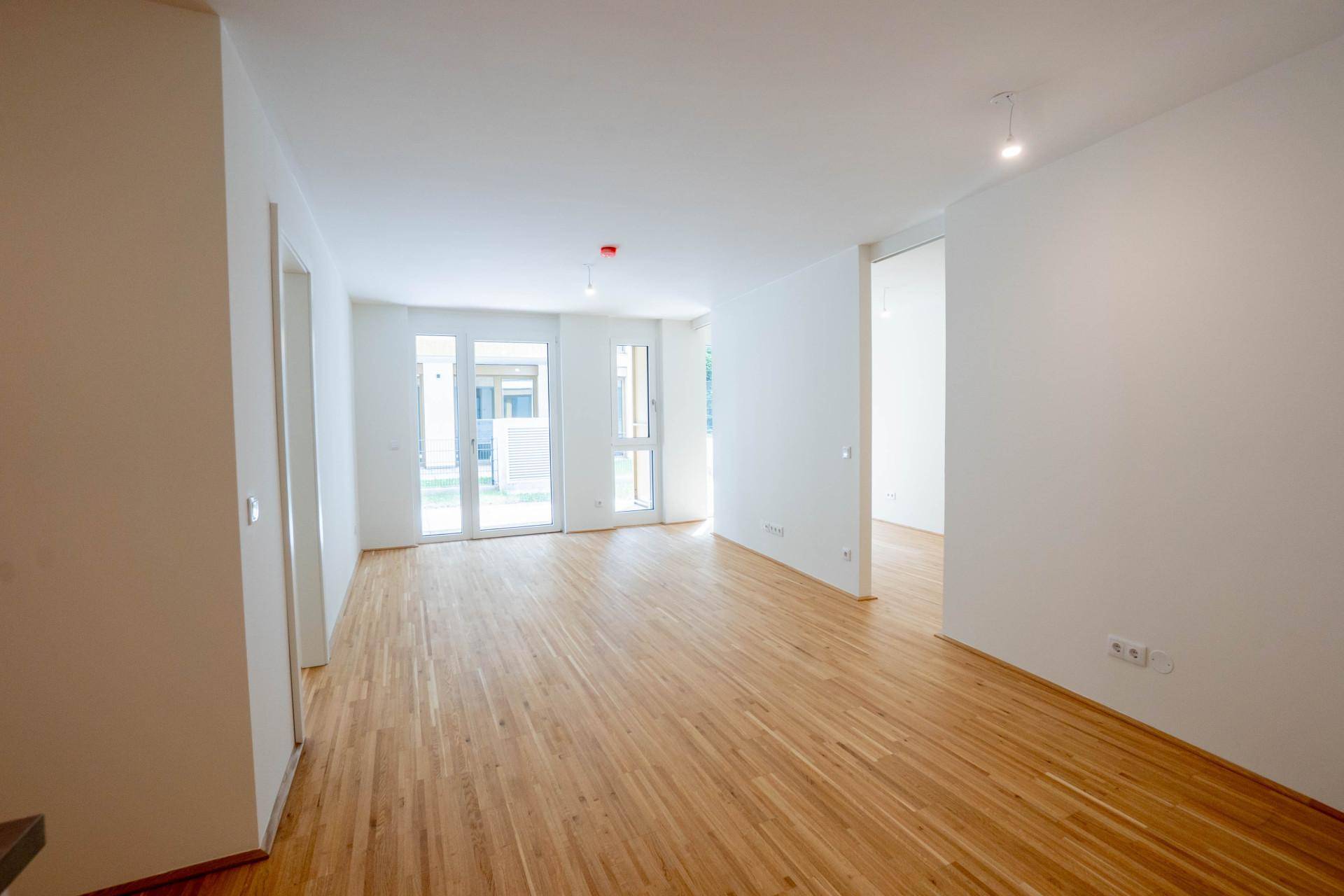 Geräumiges, helles Wohnzimmer mit Holzboden und Zugang zu einem Außenbereich durch große Fenster.