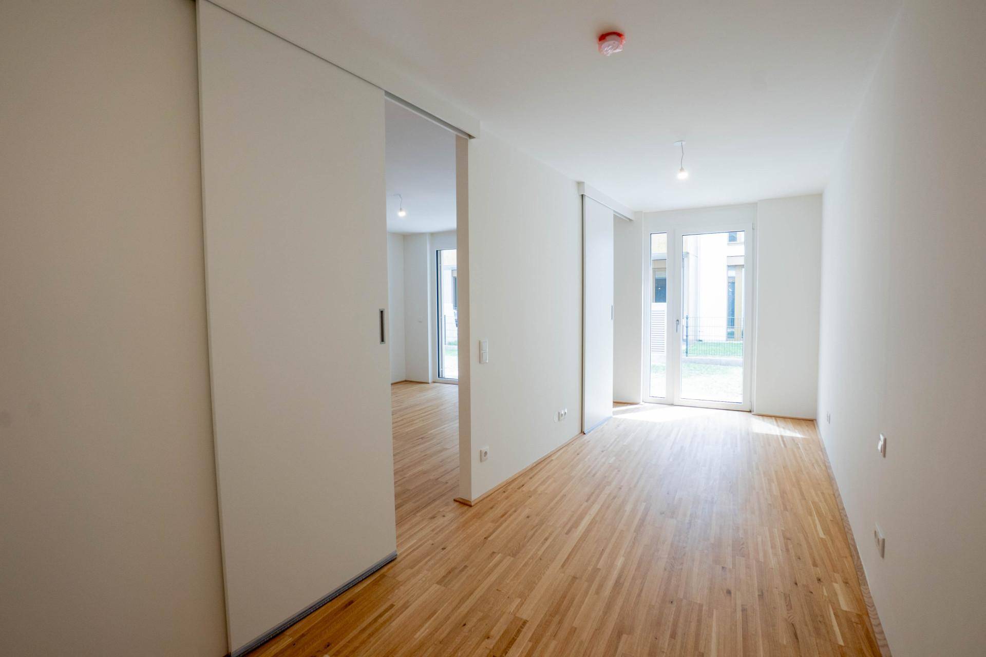 Heller Flur mit Holzboden und Schiebetüren, der zu weiteren Räumen und einem Außenbereich führt.