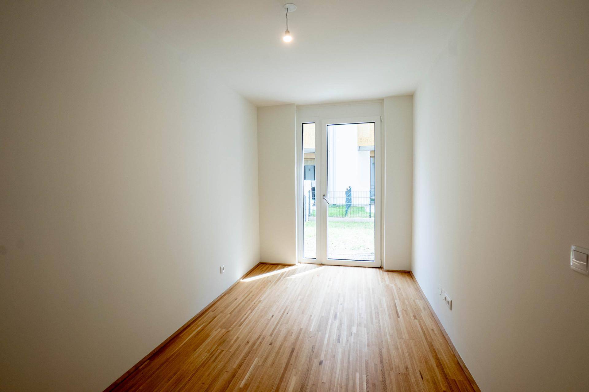 Helles Schlafzimmer mit Holzboden und direktem Zugang zu einem Außenbereich durch eine Glastür.
