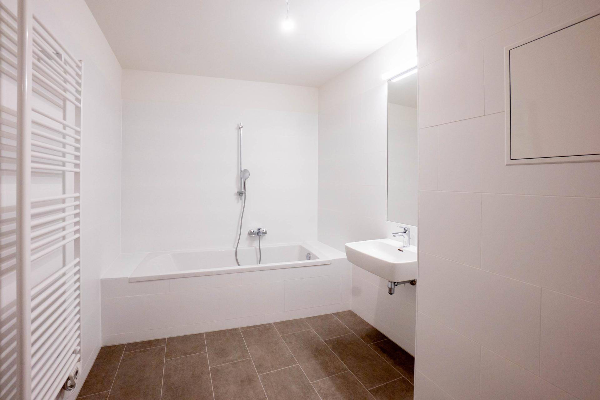 Modernes Badezimmer mit Badewanne, Waschbecken, Fliesenboden und einem beheizten Handtuchhalter.