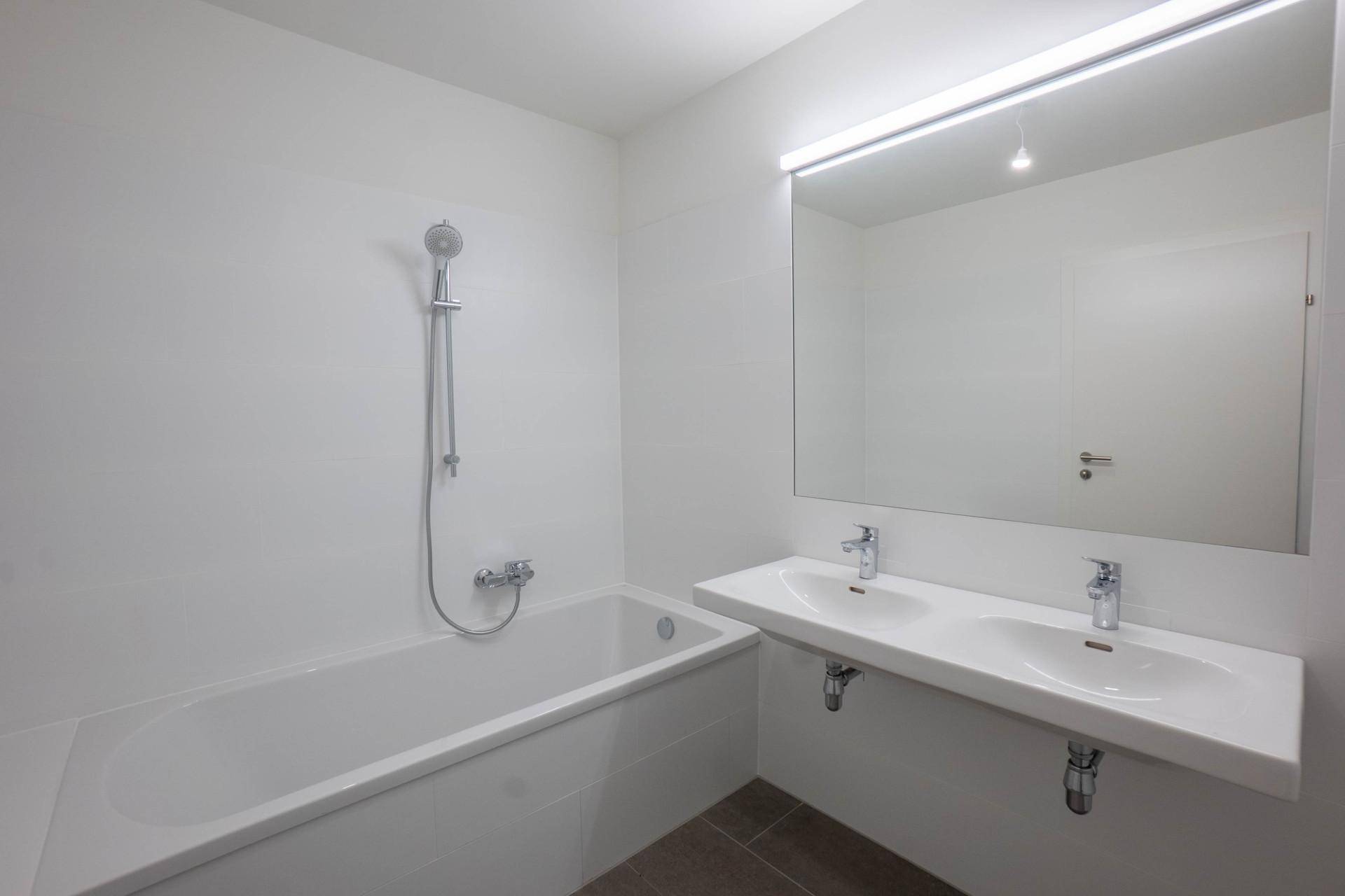 Modernes Badezimmer mit Badewanne, Doppelwaschbecken und großem Spiegel.
