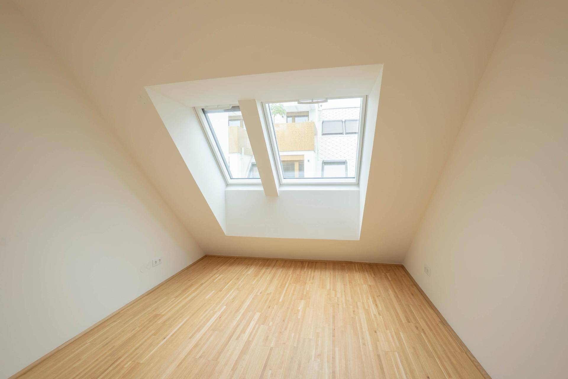 Helles Zimmer im Dachgeschoss mit Holzboden und zwei großen Dachfenstern.