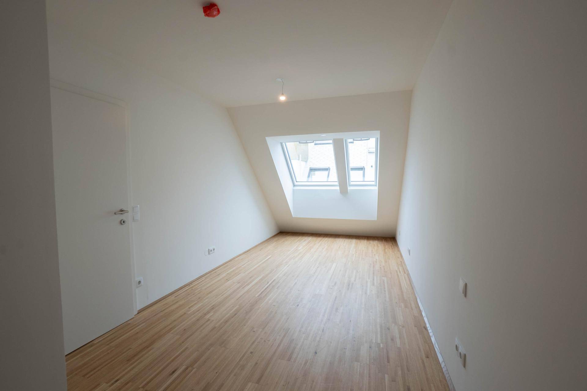 Geräumiges Zimmer im Dachgeschoss mit Holzboden und einem großen Dachfenster.