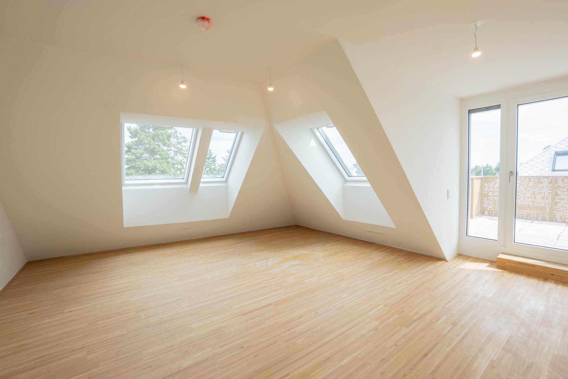 Lichtdurchfluteter Dachgeschossraum mit Holzboden, zwei Dachfenstern und Zugang zur Terrasse.