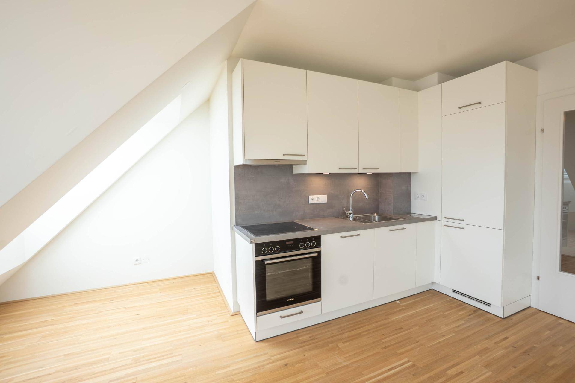 Moderne Küchenzeile mit weißen Schränken, integriertem Backofen und Kochfeld im Dachgeschoss.