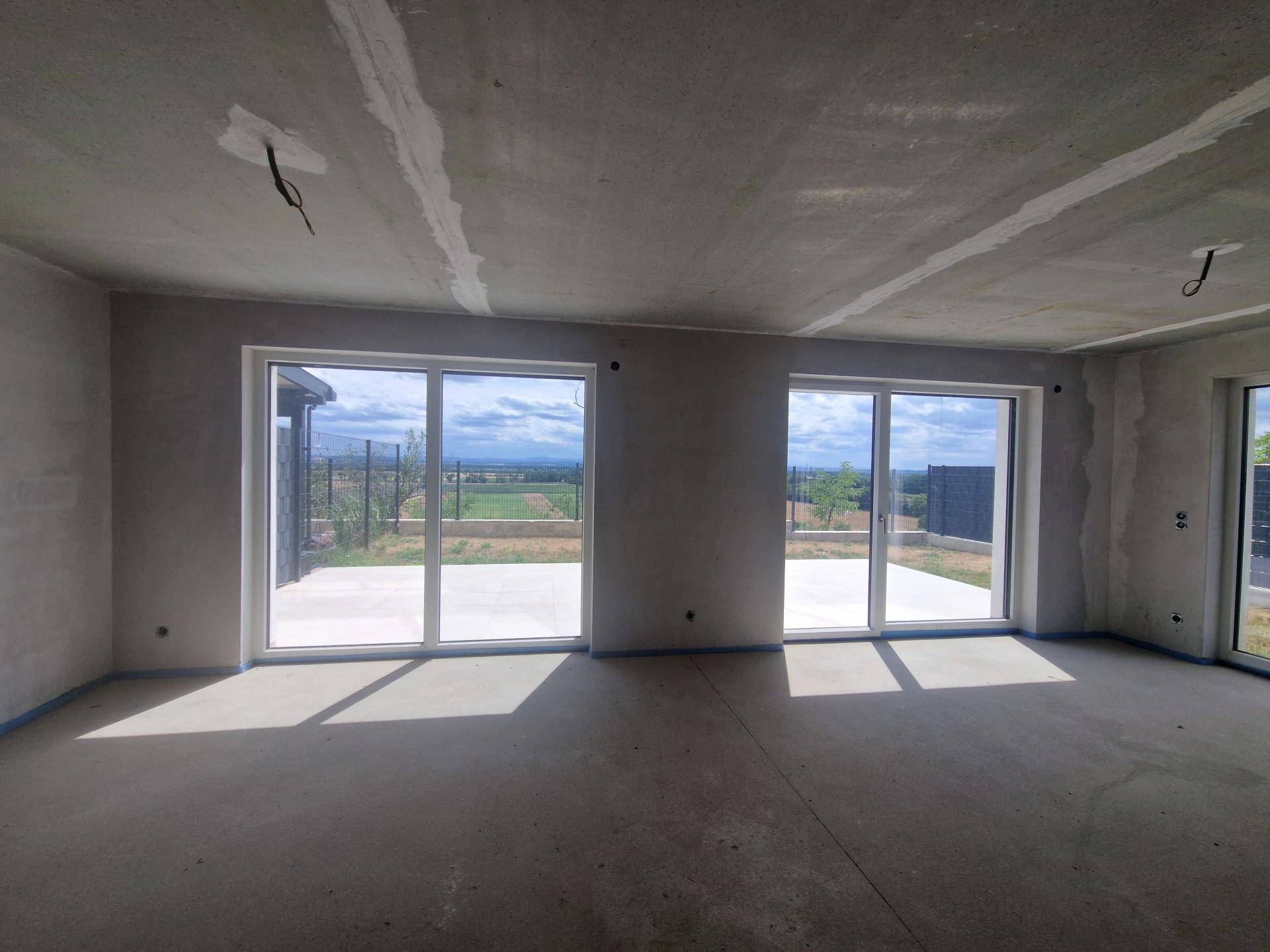 Unfertiger Wohnraum mit großen Fenstern, die einen weiten Blick auf die Landschaft bieten.
