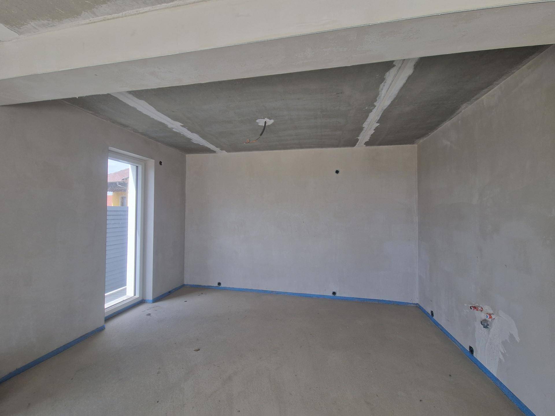 Unfertiges Zimmer mit einem Fenster und Rohbauwänden, bereit für den Innenausbau.