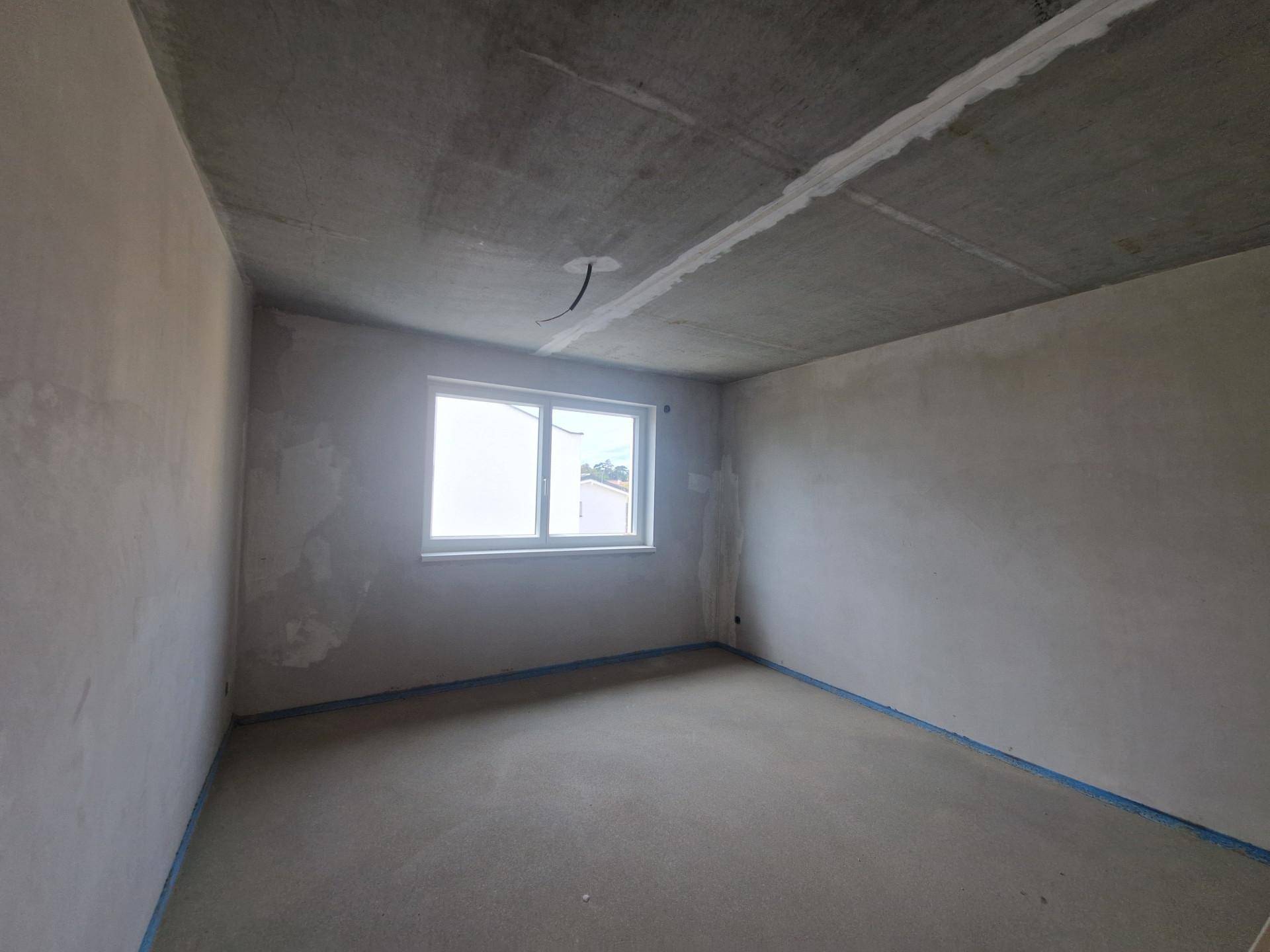 Unfertiges Schlafzimmer mit einem Fenster und Rohbauwänden, bereit für den Ausbau.