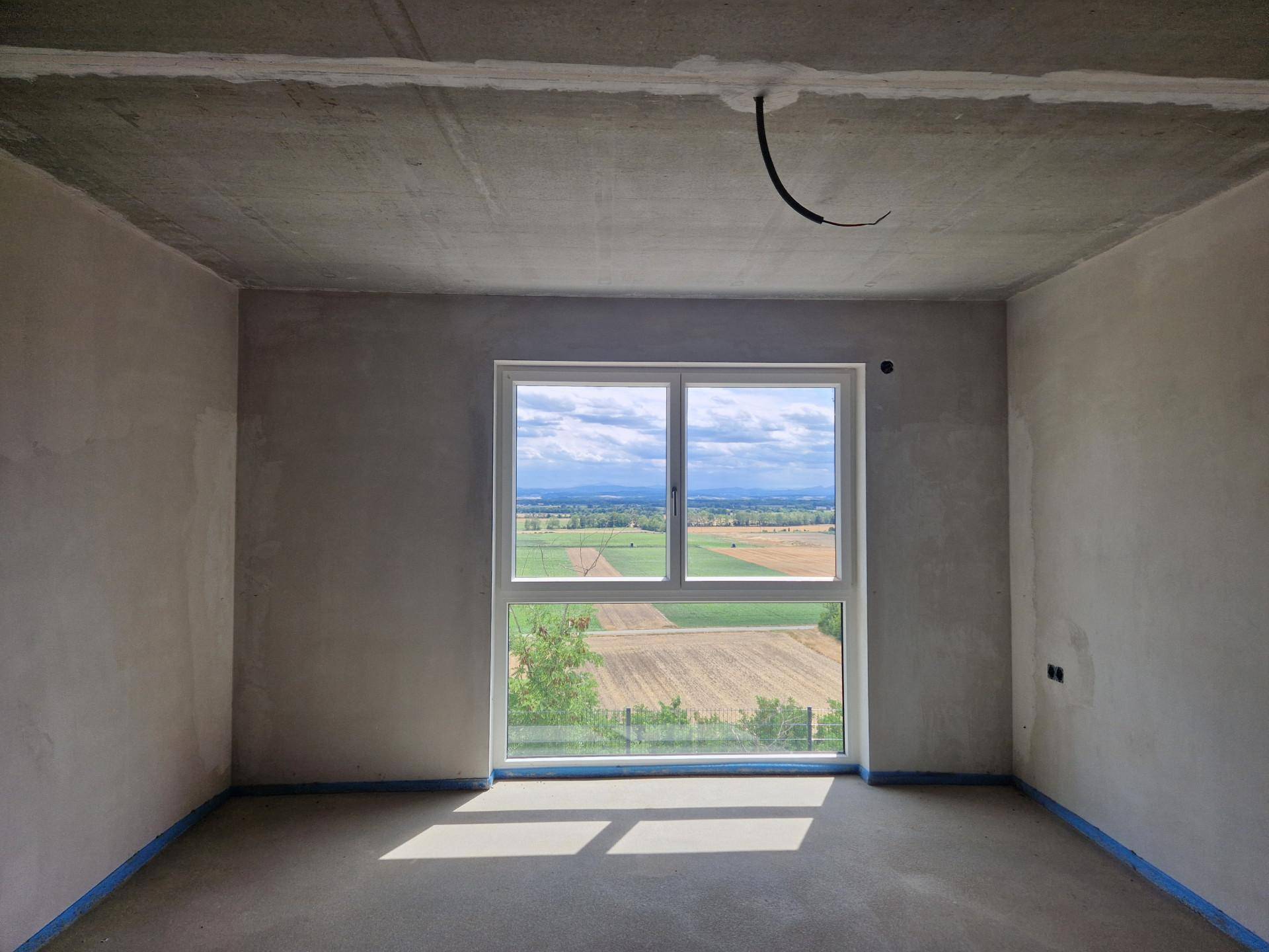 Unfertiges Zimmer mit großem Fenster und weitem Blick auf die grüne Landschaft.