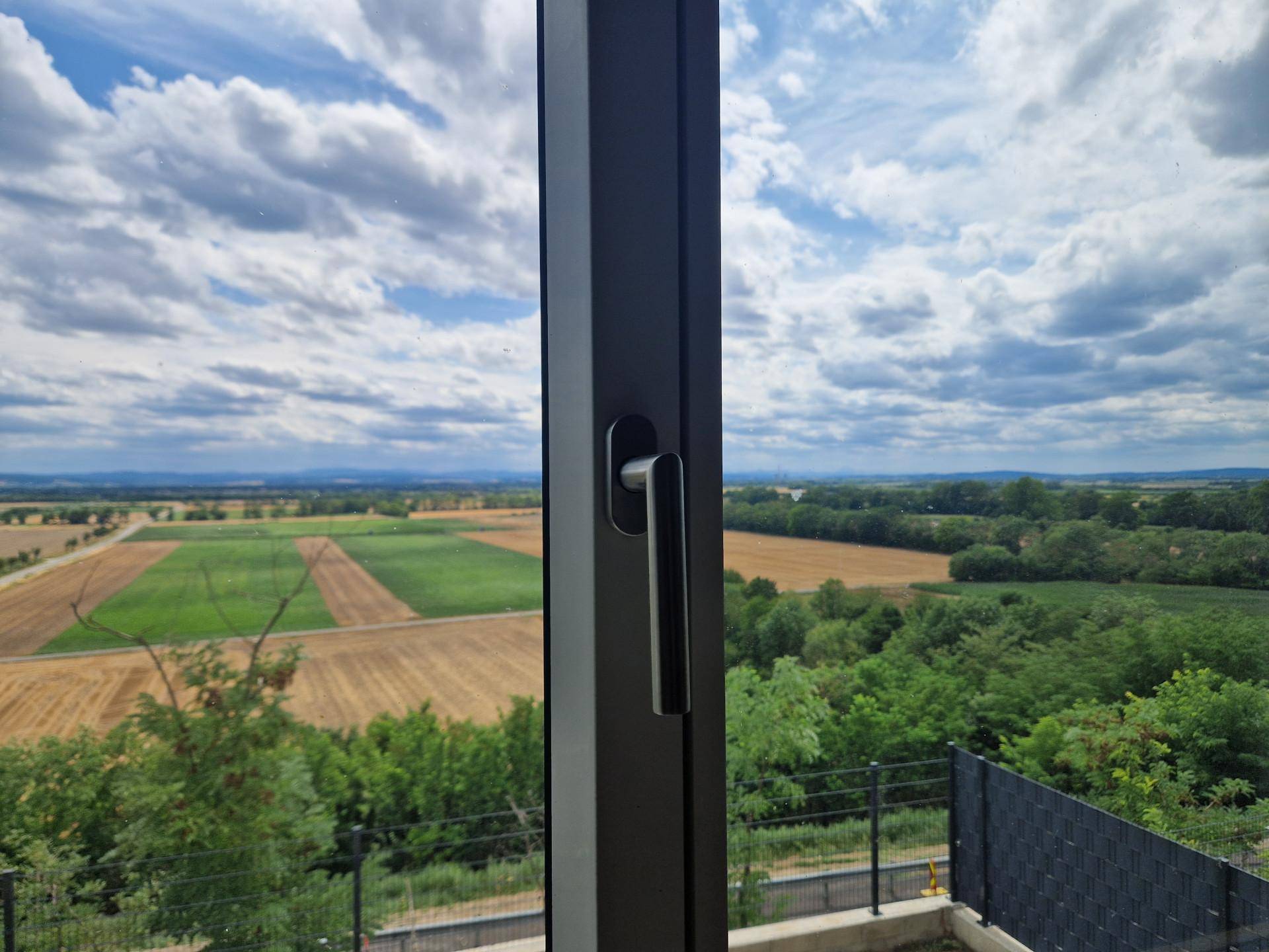 Weitläufiger Ausblick aus dem Fenster auf die ländliche Umgebung mit Feldern und Bäumen.
