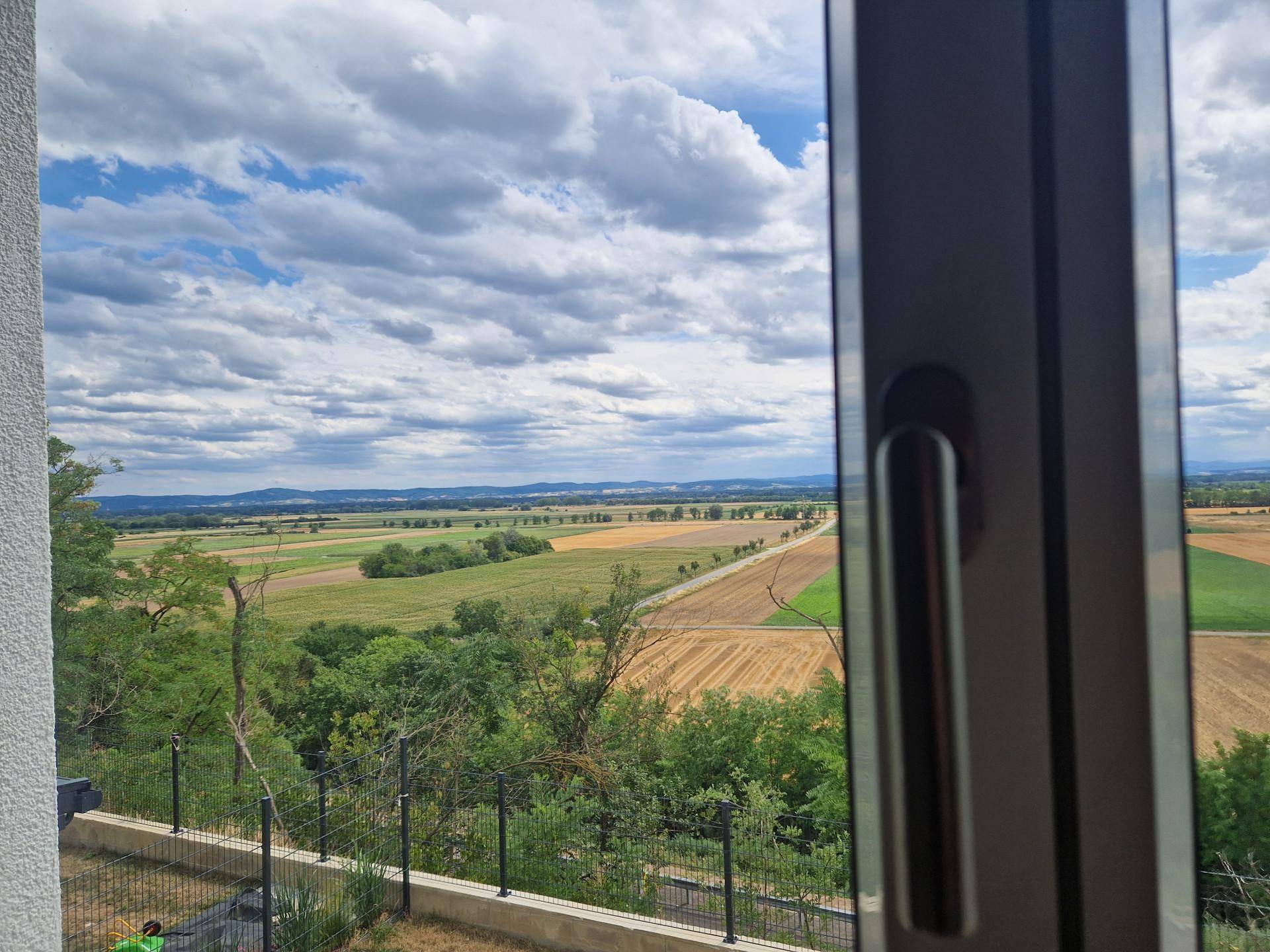 Blick aus dem Fenster auf die weite Landschaft mit Feldern und einem Horizont unter Wolken.