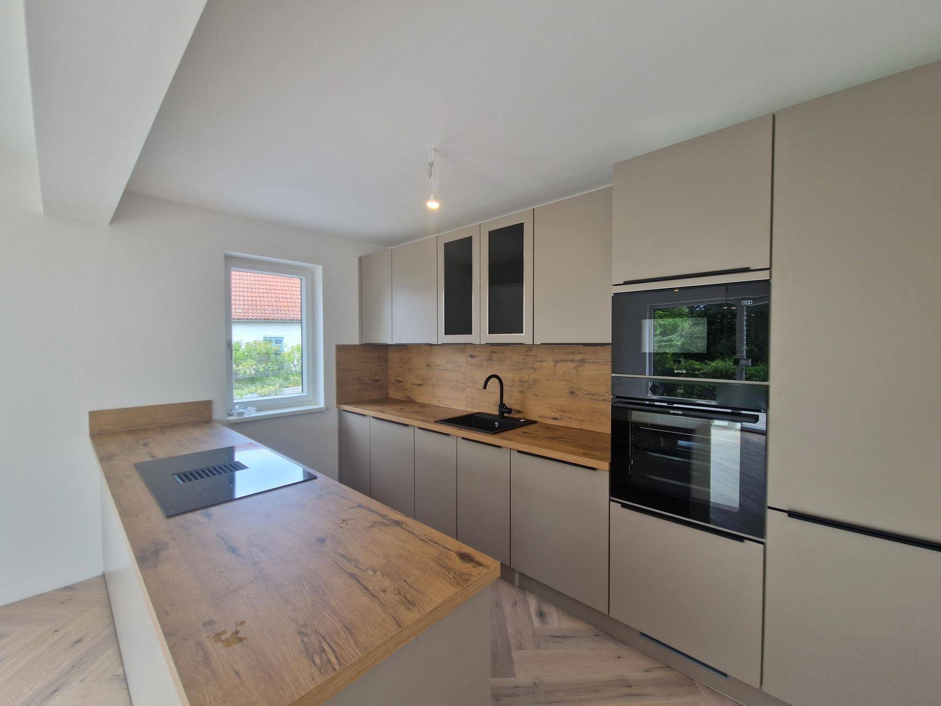 Moderne Einbauküche mit holzfarbener Arbeitsplatte, Induktionskochfeld und integrierten Geräten.