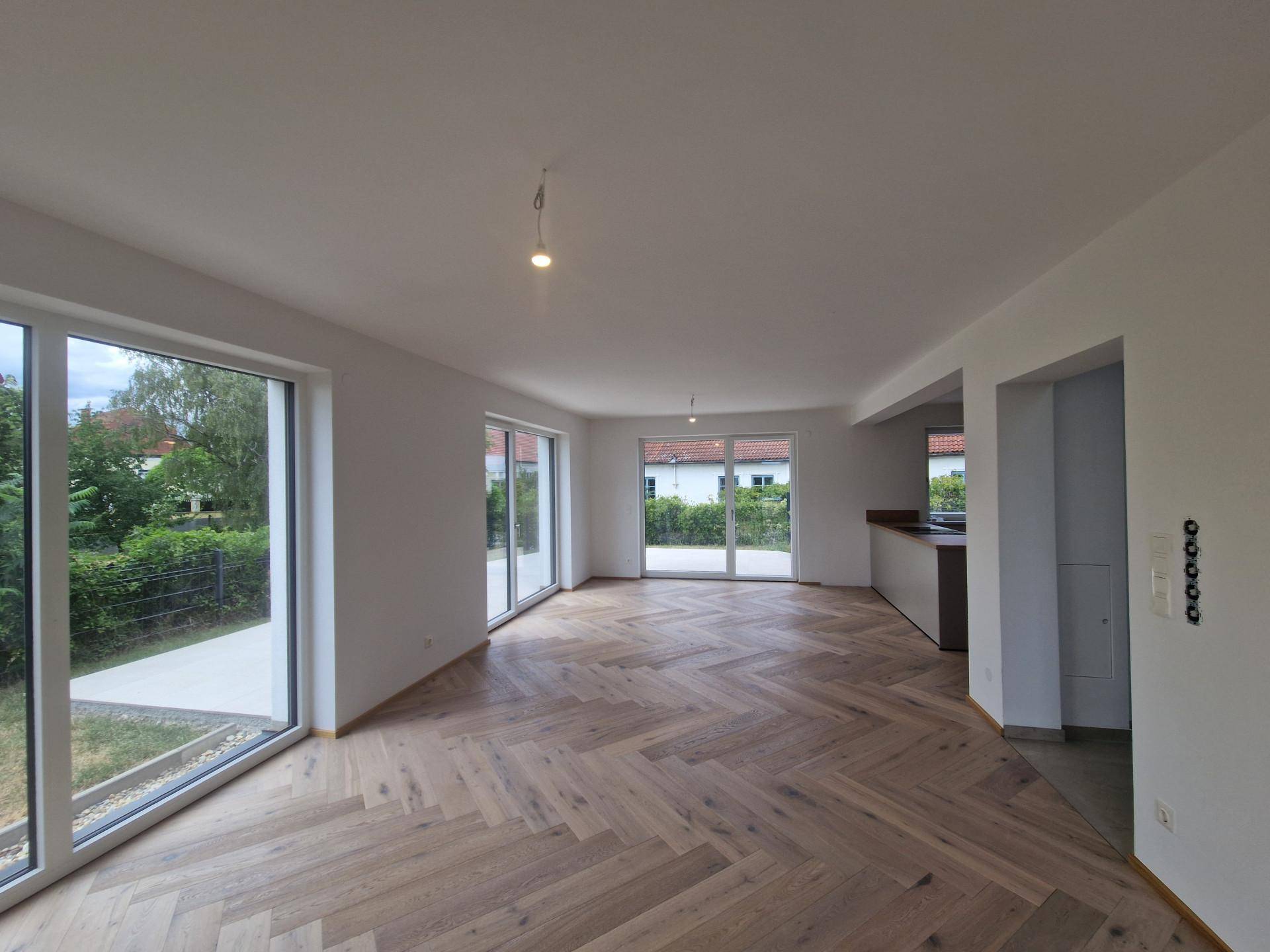 Geräumiger Wohnbereich mit Fischgrätparkett und mehreren Zugängen zur Terrasse und zum Garten.