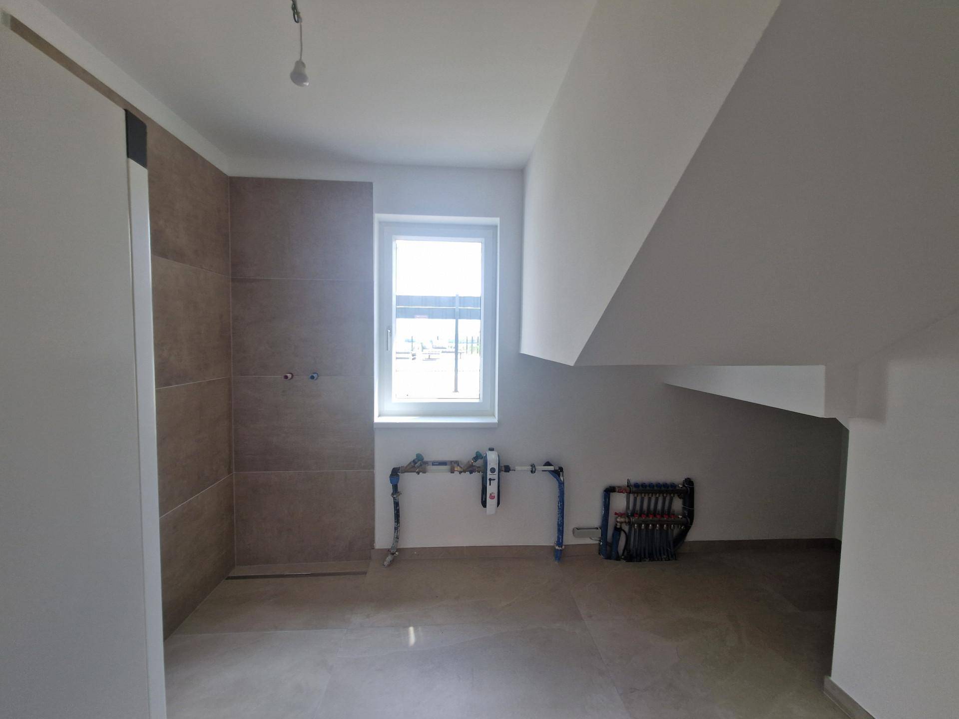 Unfertiger Raum mit Fenster, sichtbaren Installationen und Dachschräge, ideal als Hauswirtschaftsraum.