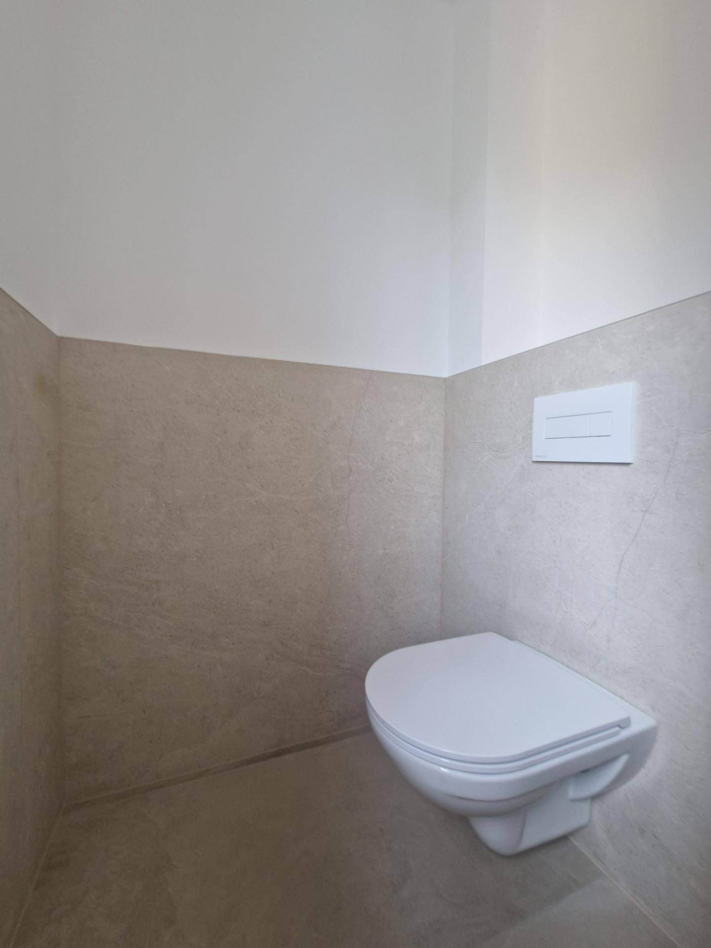 Schlichtes WC mit Wand-WC und neutralen Fliesen, in einem modernen Design.