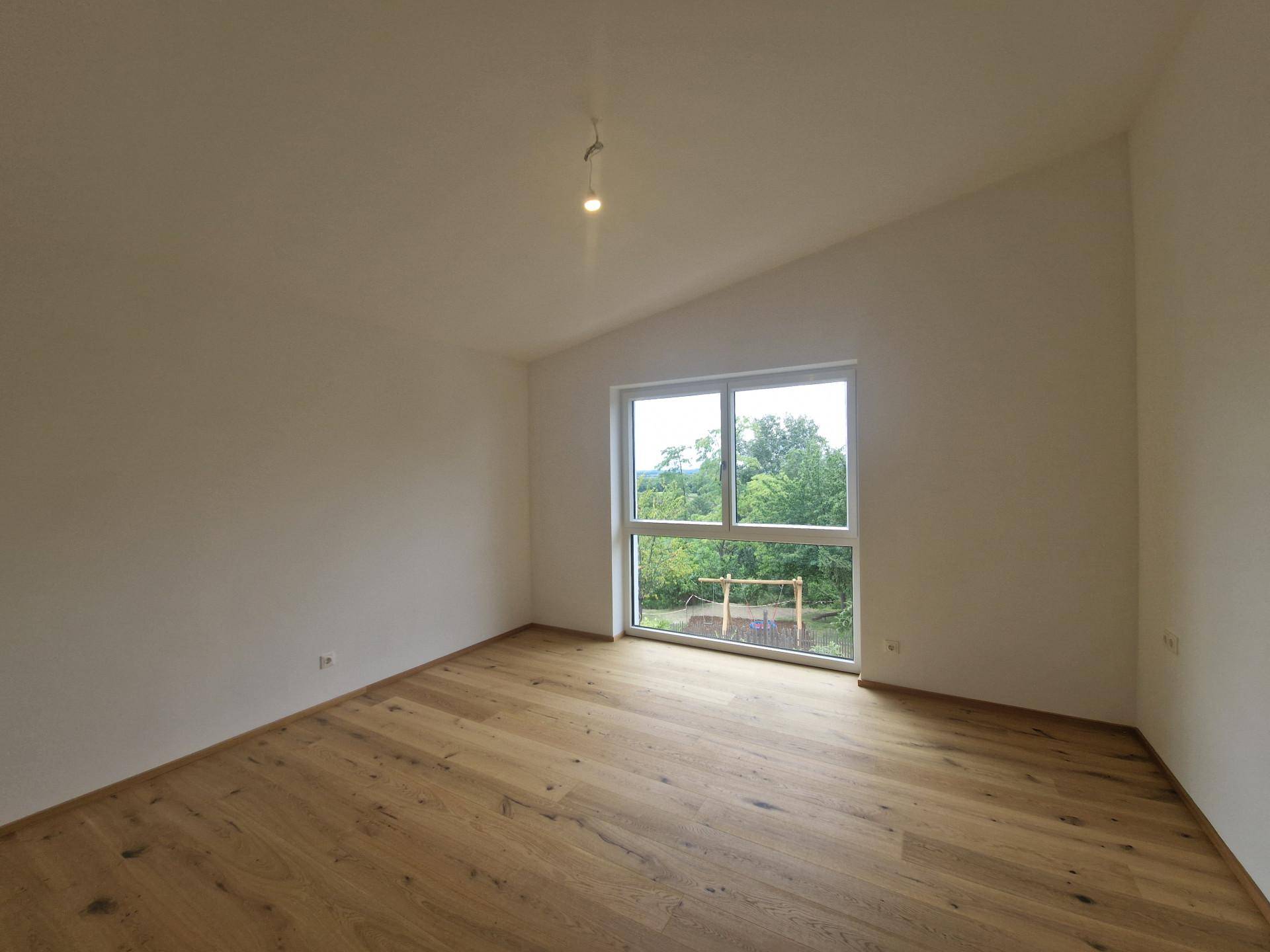Helles Schlafzimmer mit Fischgrätparkett, großer Fensterfront und Dachschräge.