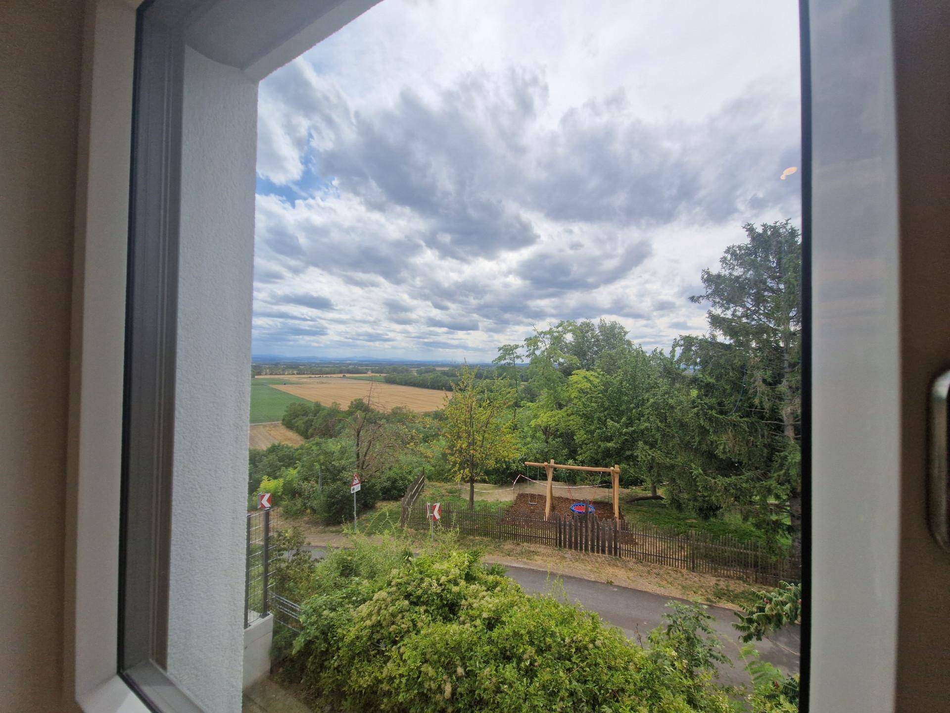 Weitläufiger Ausblick aus dem Fenster über Felder, Bäume und einen Spielplatz.