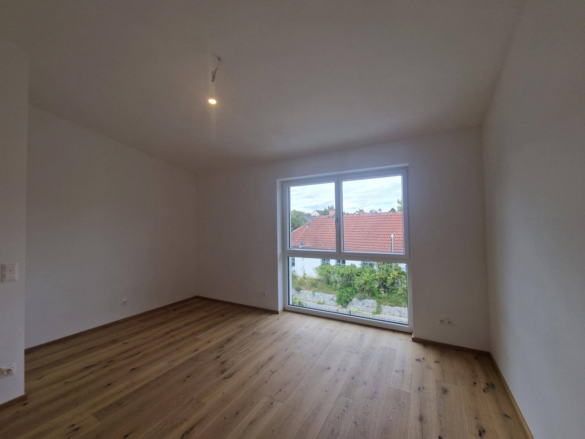 Geräumiges Schlafzimmer mit Fischgrätparkett und großem Fenster mit Blick auf die Umgebung.