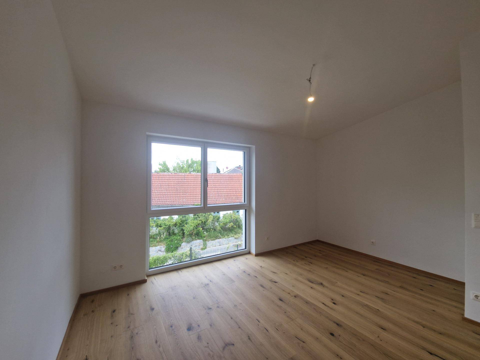 Helles Schlafzimmer mit Fischgrätparkett und großem Fenster, das viel Tageslicht hereinlässt.