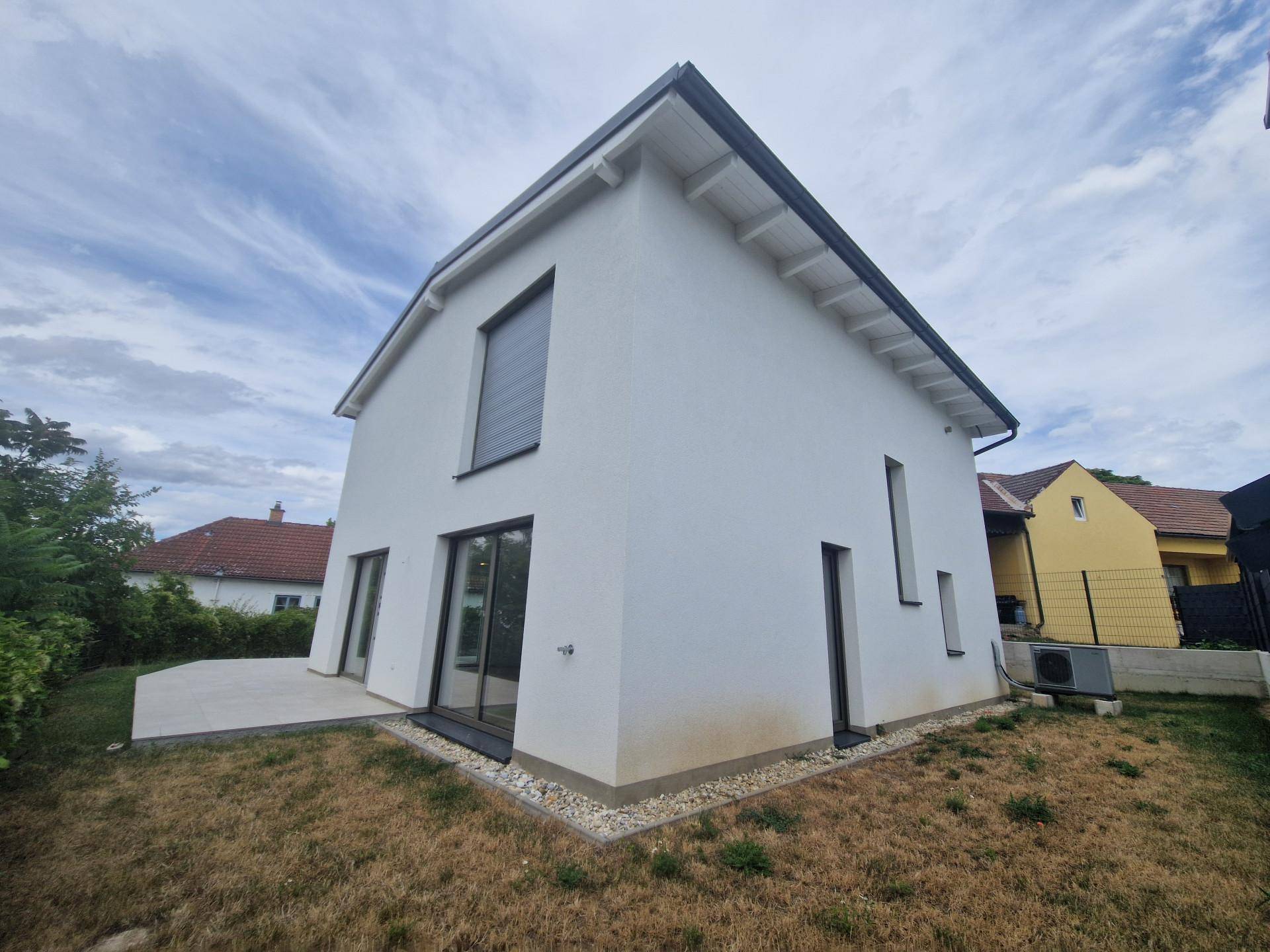 Rückseite des Hauses mit kleiner Terrasse und Rasenfläche, umgeben von Grün.