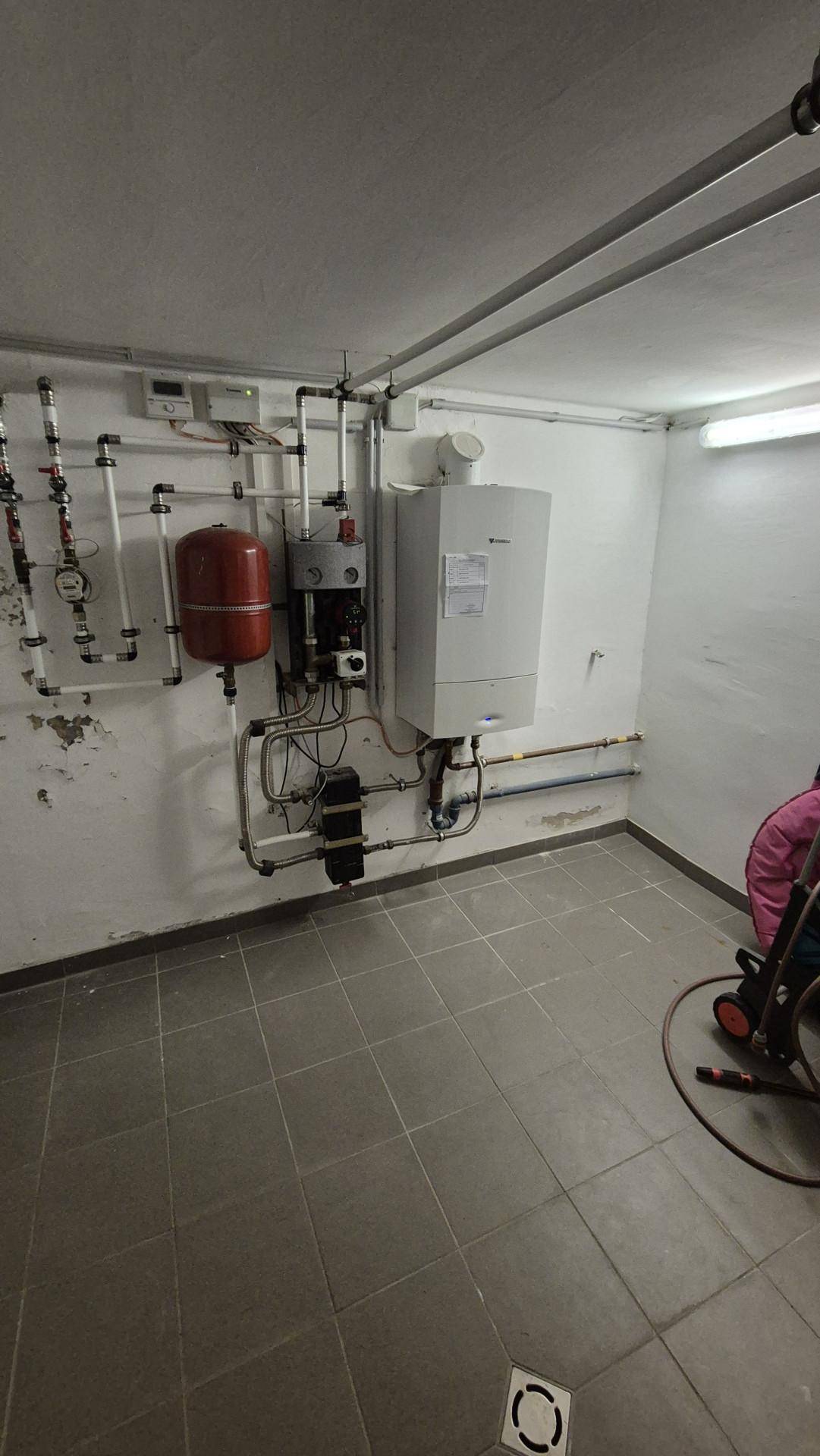 Technikraum im Keller mit Heizungsanlage und sichtbaren Rohrleitungen.
