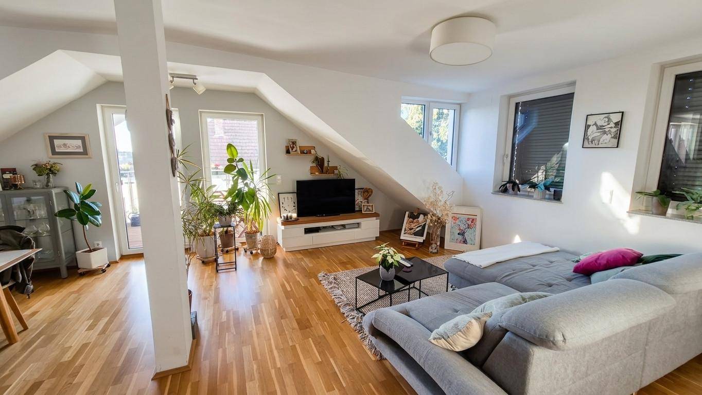 Gemütliches Wohnzimmer im Dachgeschoss mit Schrägen, Holzboden und Zugang zum Balkon.