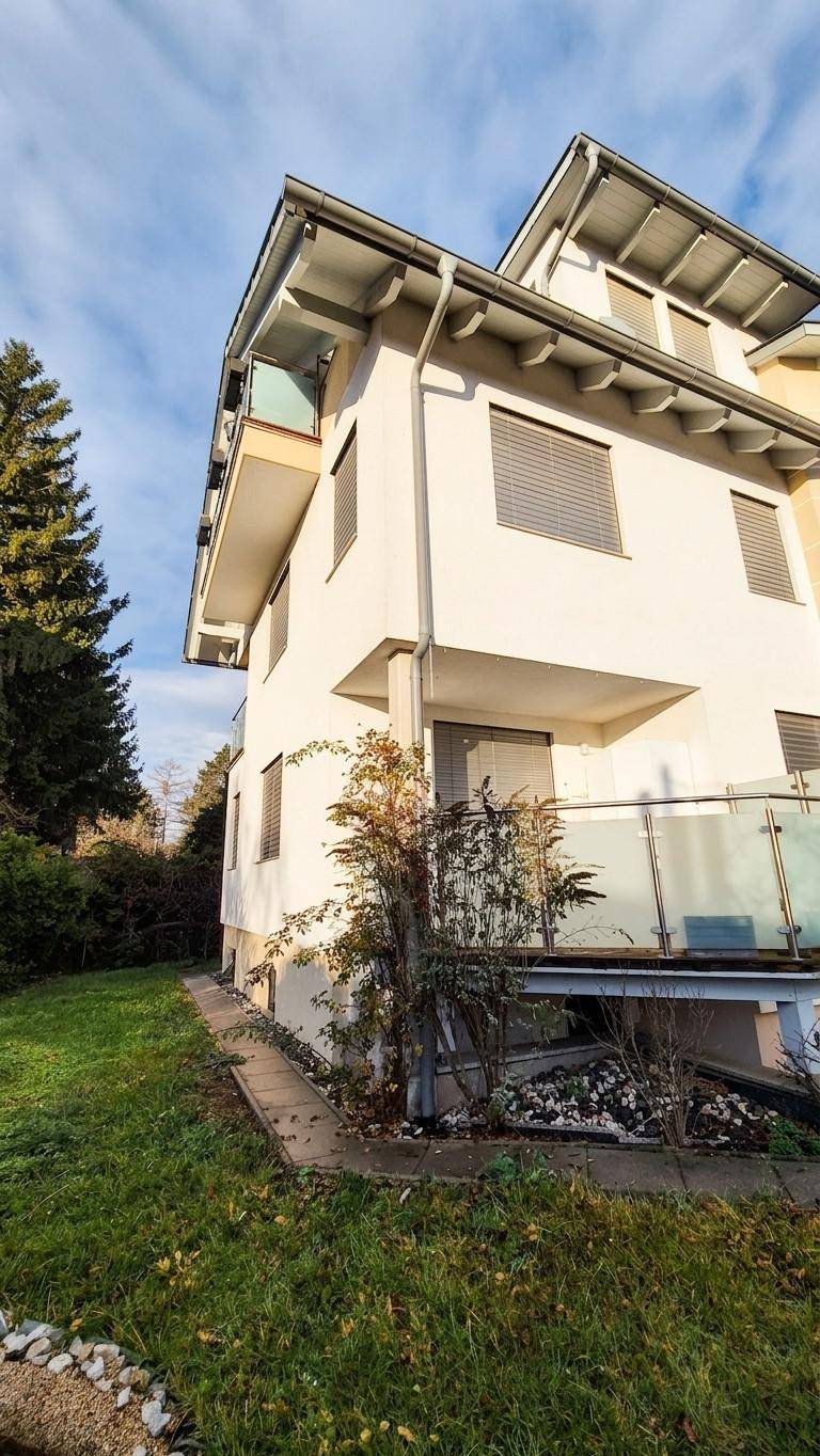 Seitenansicht des Hauses mit Balkonen, Rollläden und einem kleinen Grünbereich.