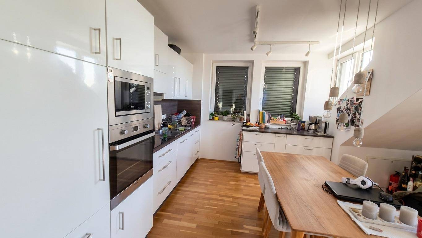 Moderne Küche mit Essbereich, weißen Hochglanzfronten und Holzboden.