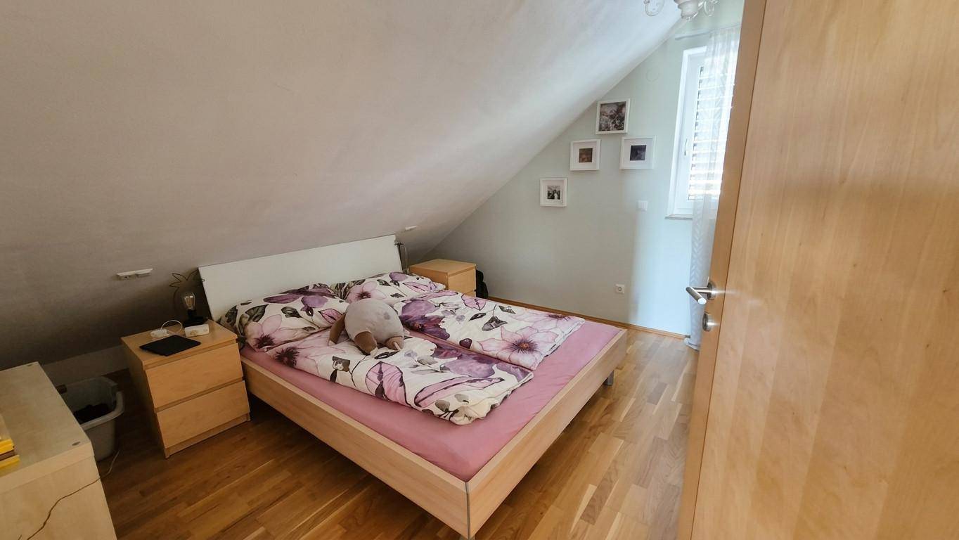 Schlafzimmer im Dachgeschoss mit Holzboden, schrägen Wänden und einem Fenster.