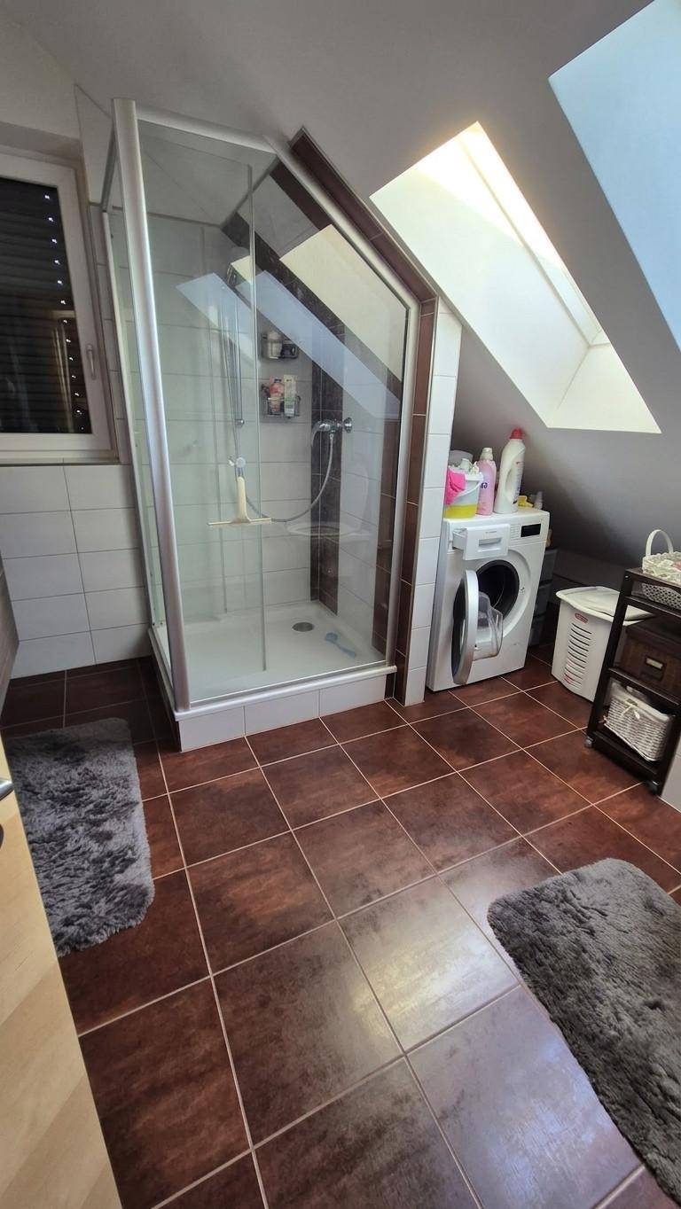Badezimmer im Dachgeschoss mit Dusche, Waschmaschine und Dachfenster.