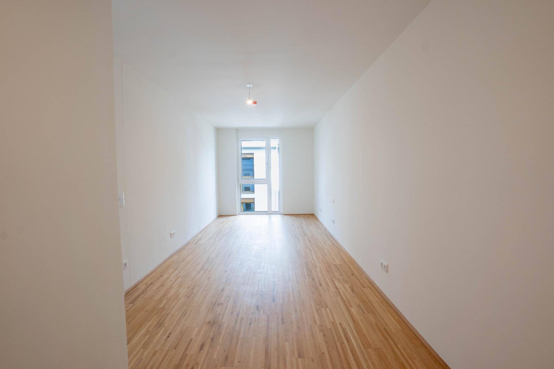 Langer, heller Raum mit Holzboden und Fenster am Ende, ideal als Schlafzimmer oder Büro.