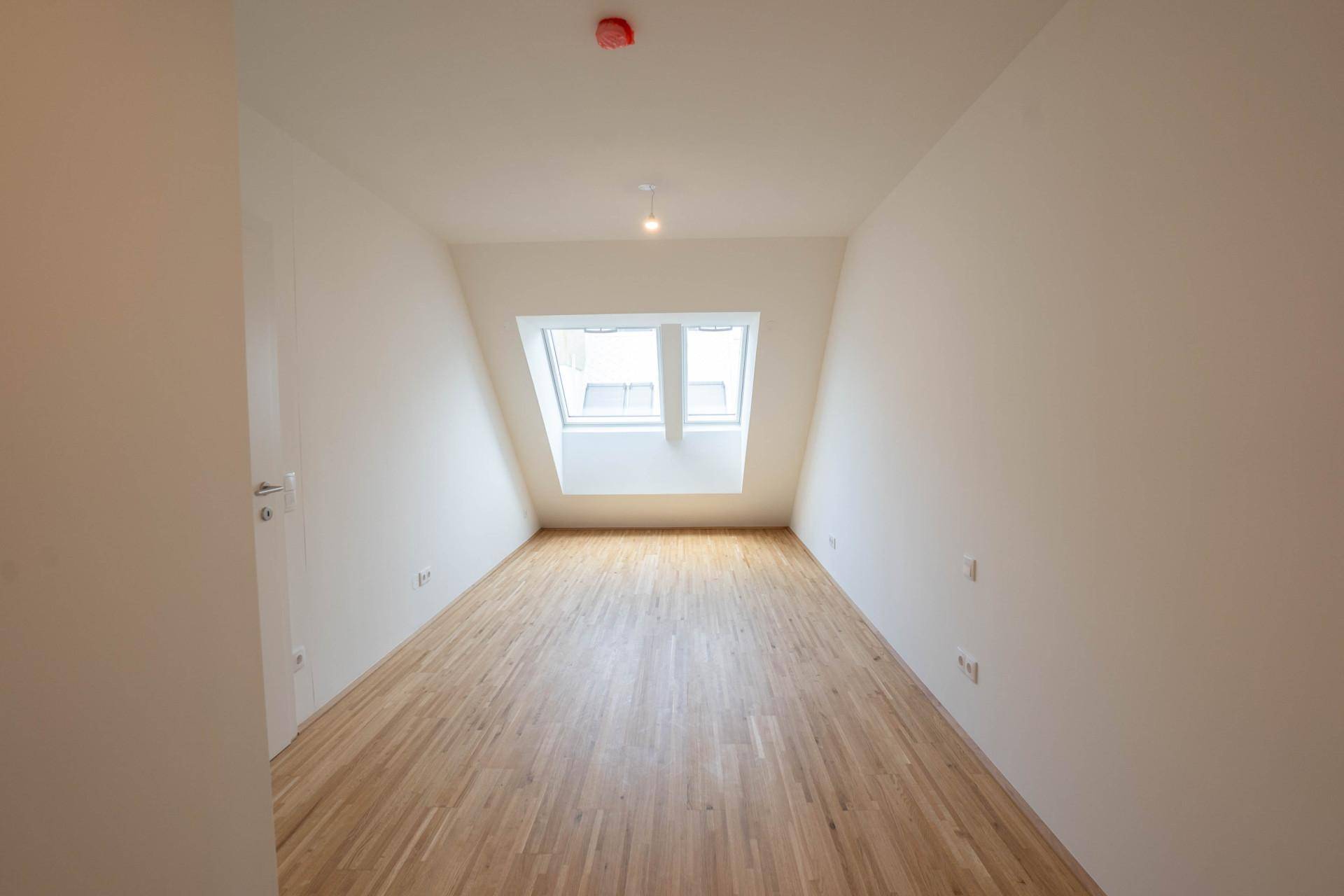 Geräumiges Zimmer mit Holzboden, Dachschräge und einem großen Dachfenster.