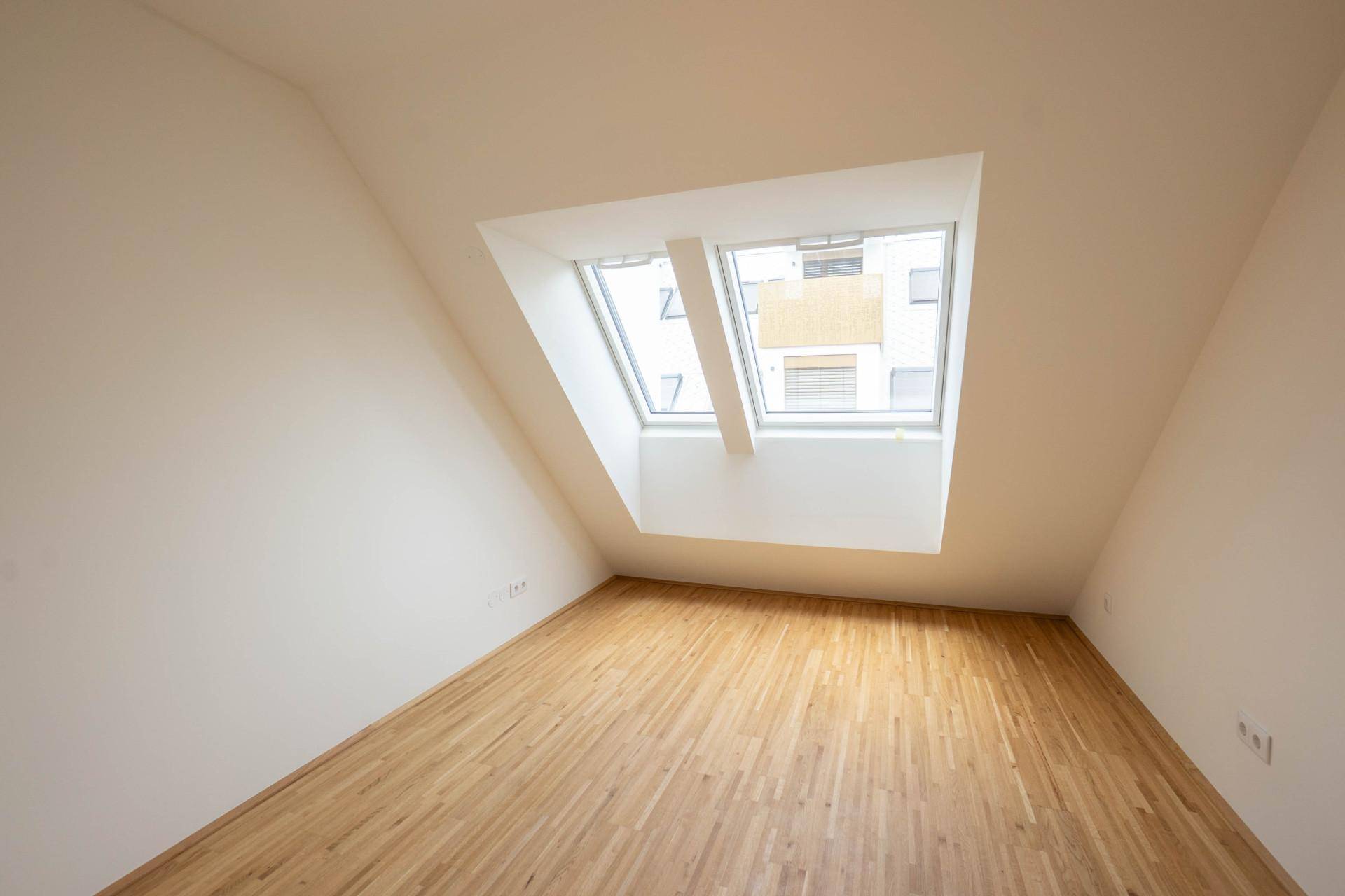 Helles Zimmer mit Holzboden, Dachschräge und großem Dachfenster für viel Tageslicht.