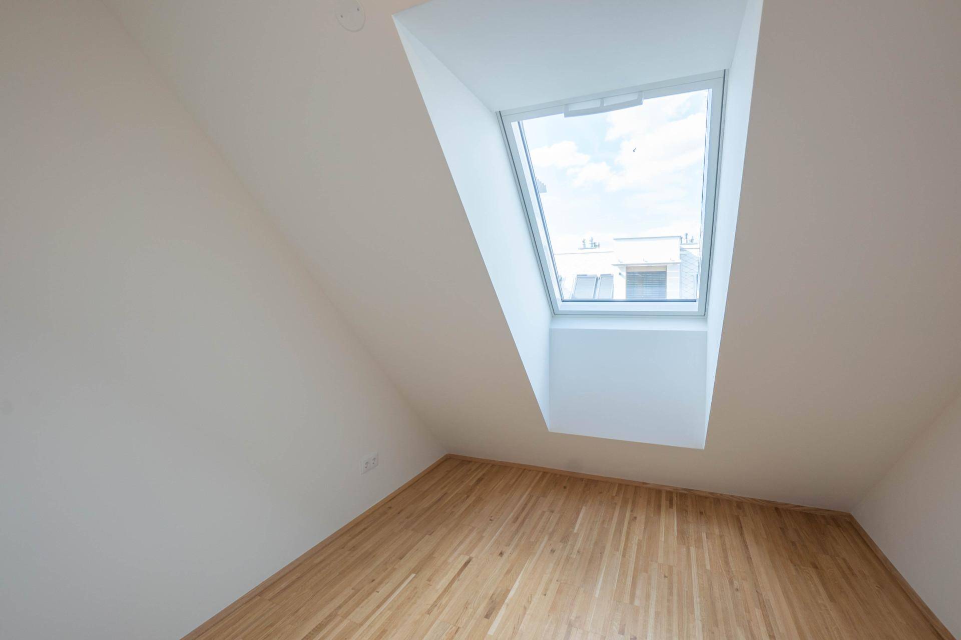 Gemütliches Dachzimmer mit einem großen Dachfenster, schräger Decke und warmem Holzfußboden.