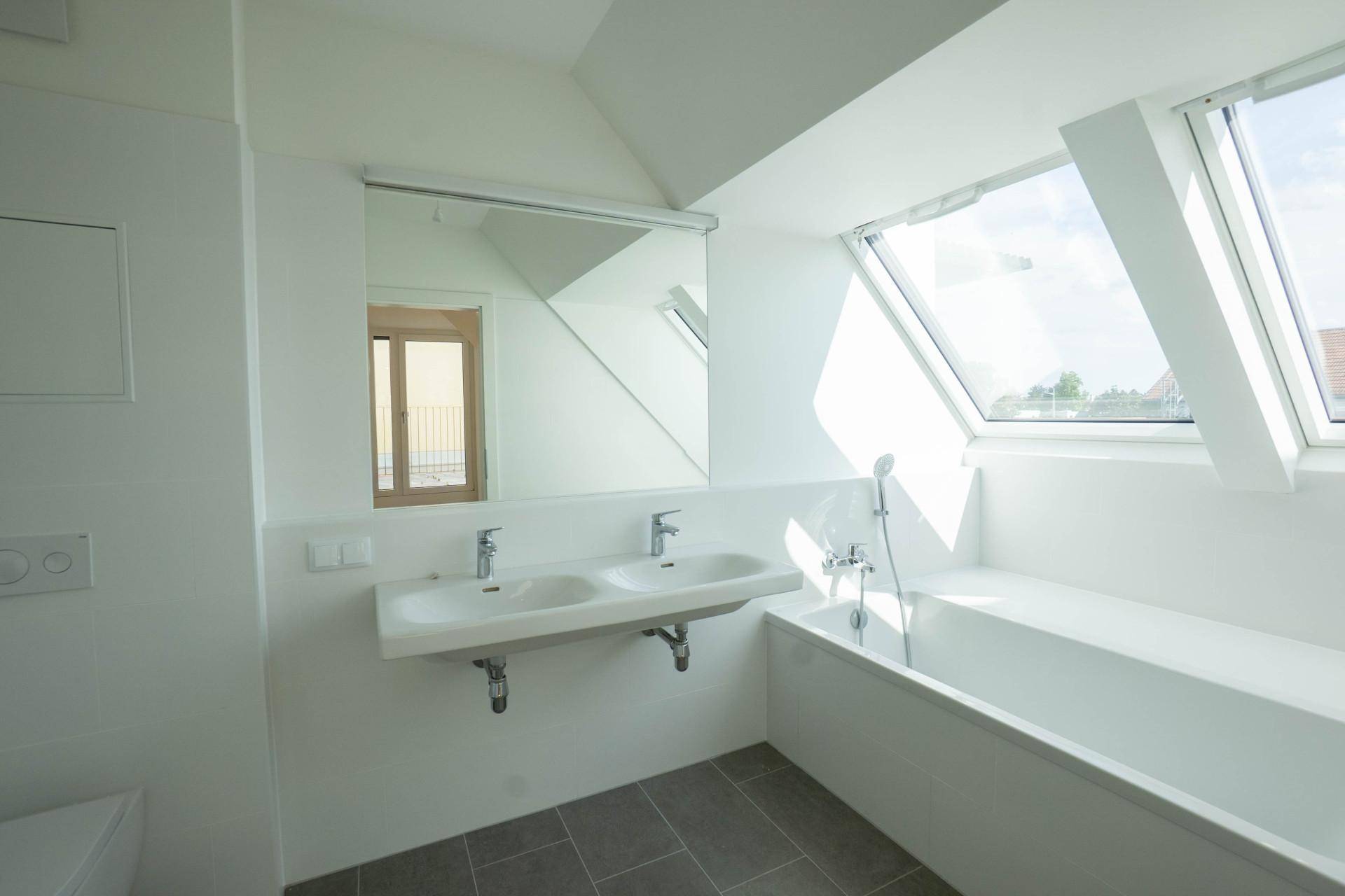 Modernes Badezimmer mit Doppelwaschbecken, Badewanne und hellen Dachfenstern unter schräger Decke.