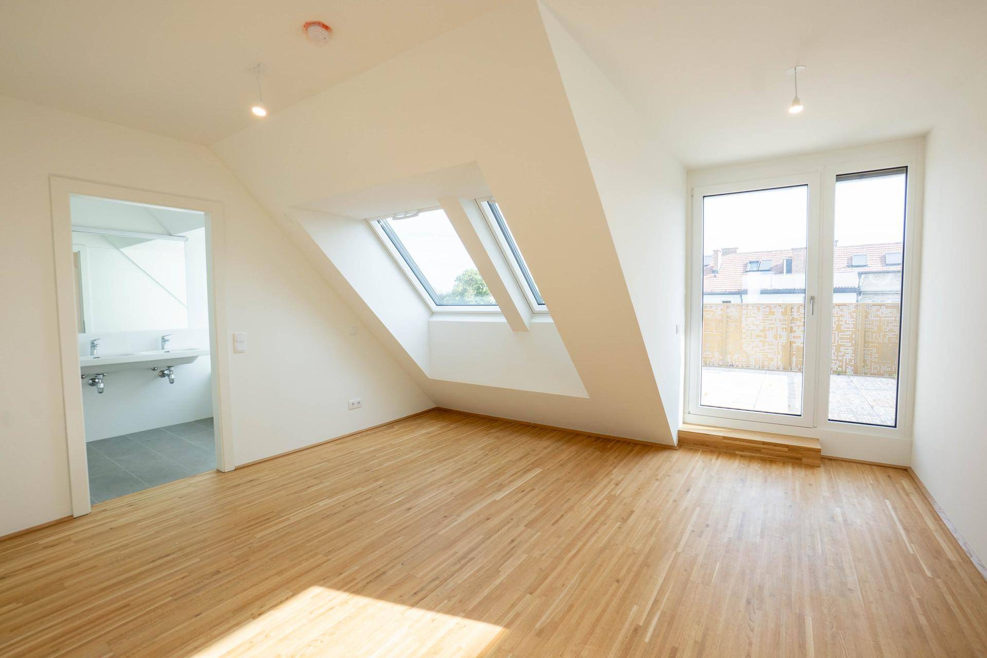 Helles Schlafzimmer im Dachgeschoss mit Dachfenstern, Holzfußboden und direktem Zugang zum Badezimmer.