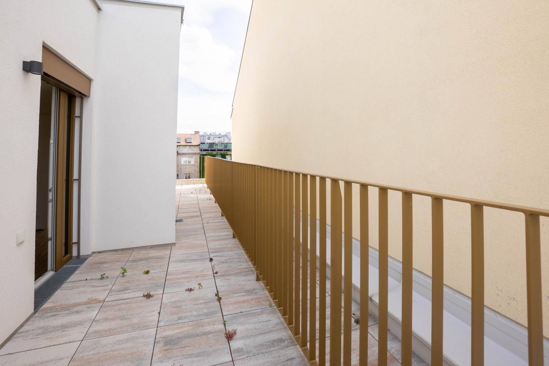 Langer, schmaler Balkon mit einfachem Metallgeländer und Fliesenboden, ideal für Entspannung.